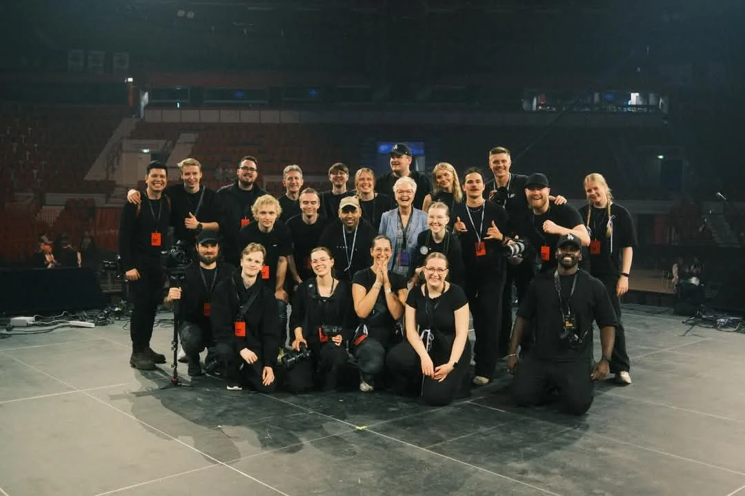 Group of people, possibly a crew or performers, on stage in a large auditorium or theater, smiling and posing for the photo.