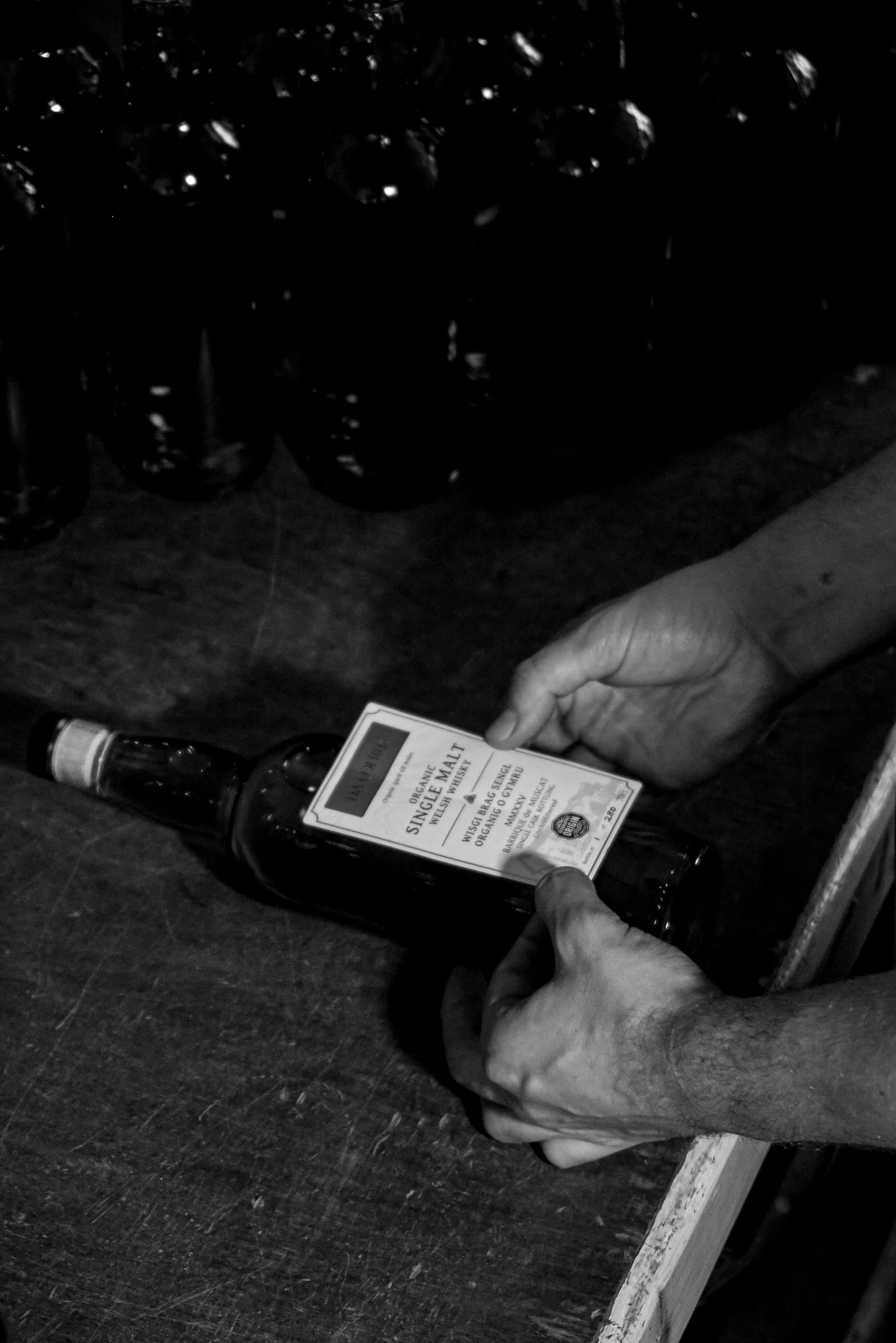 A person opening a bottle of organic beer with a wooden label, with several bottles of beer in the background on a wooden table.