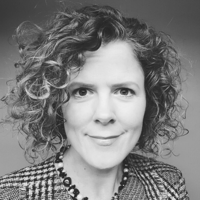 Black and white portrait of a woman with curly hair, wearing a checked blazer and a beaded necklace.