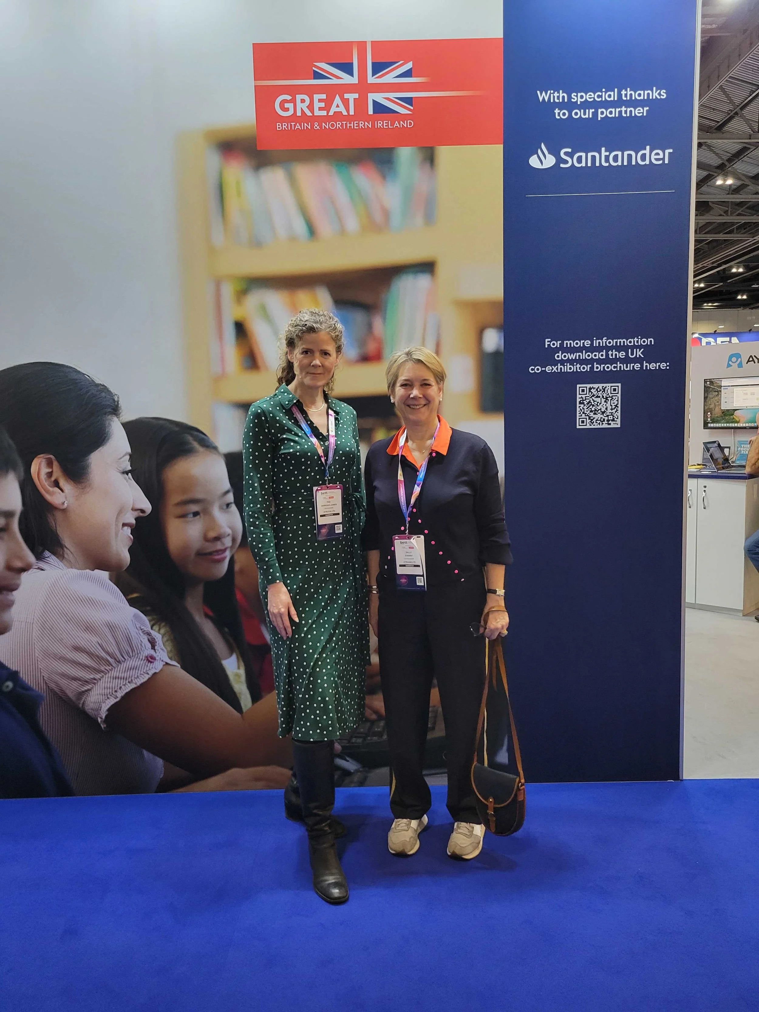 Vitruvia's co-founders standing in front of a large banner at BETT London, January 2026, with a blue background and white text. The banner has a red section with a British flag and the words "GREAT Britain & Northern Ireland". The conference setting 