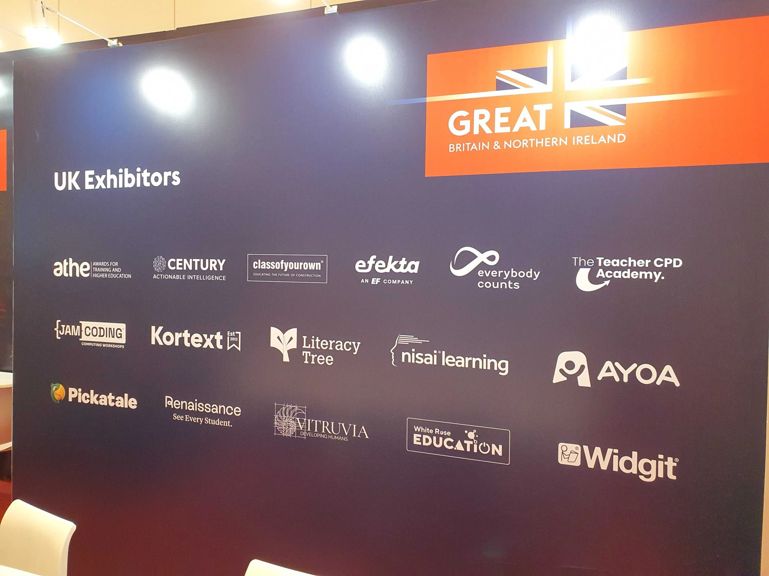At BETT a dark purple wall with several logos of companies and organizations related to education, technology, and business, along with the words 'UK Exhibitors' and the 'GREAT Britain & Northern Ireland' logo.