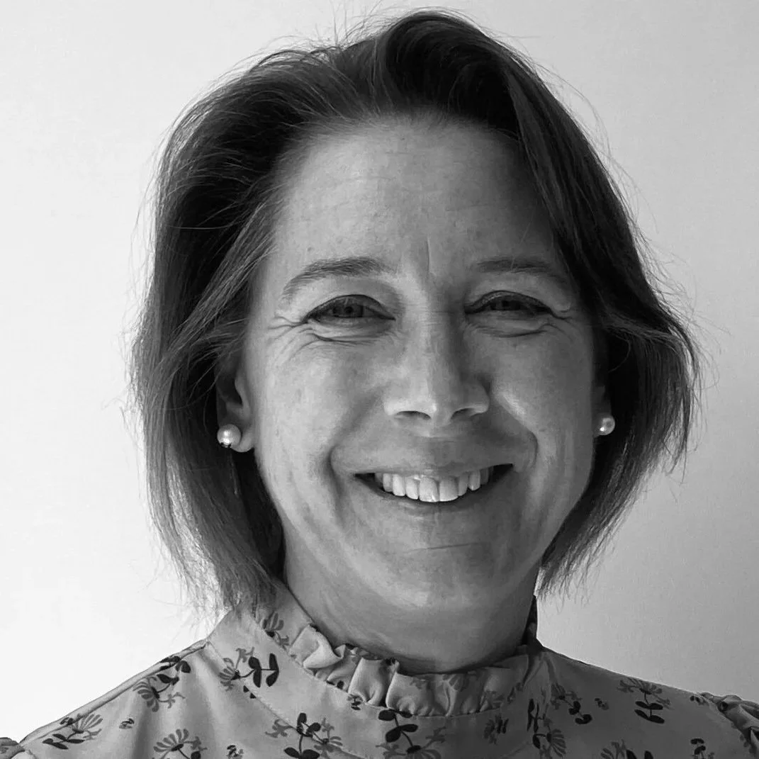 A smiling woman with short hair, pearl earrings, and a floral-patterned top in black and white.