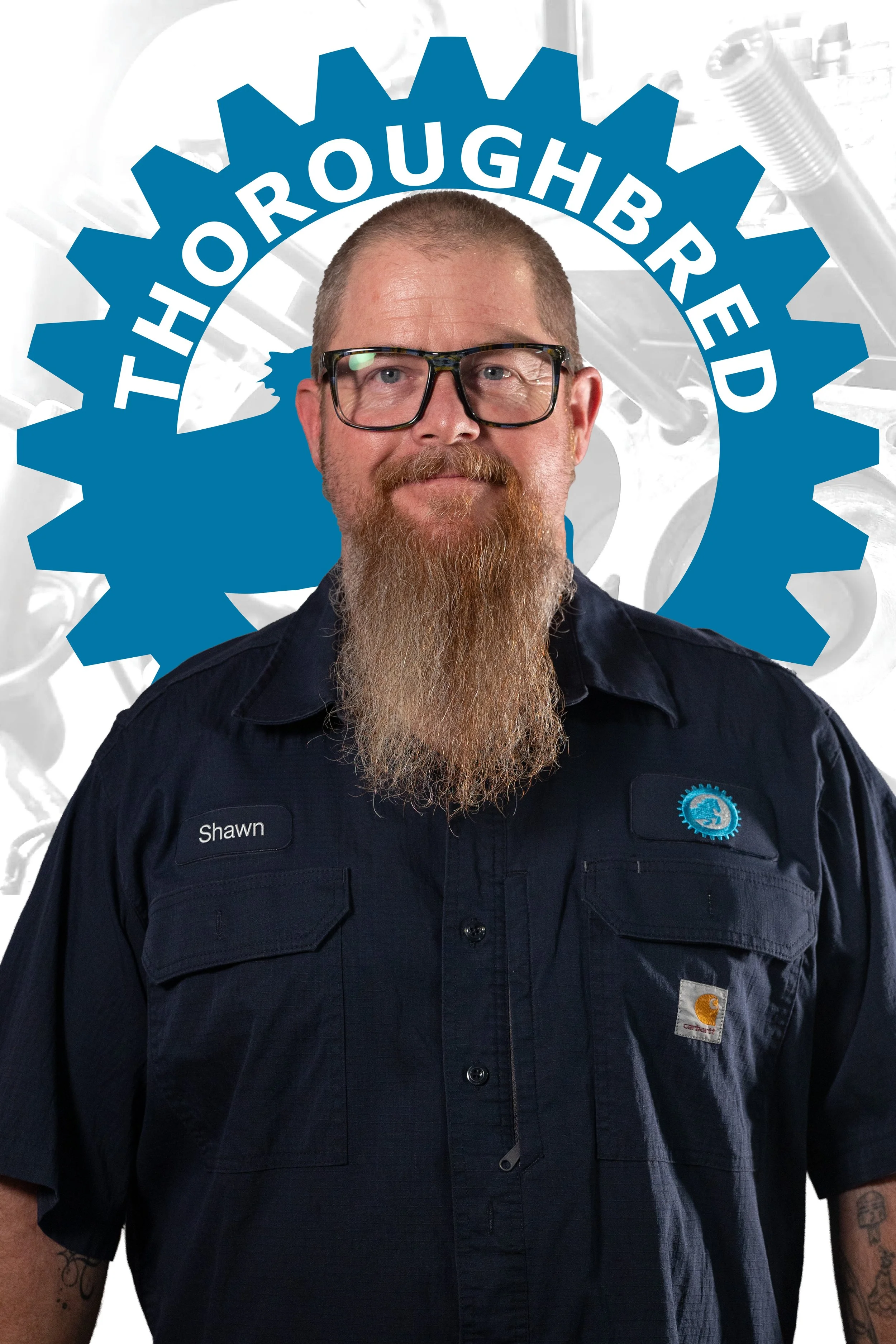 A man with glasses, a beard, and a mustache wearing a dark blue work shirt with a name tag that says 'Shawn', standing in front of a background featuring a graphic of a large blue gear and the words 'Thoroughbred Motors' in white letters