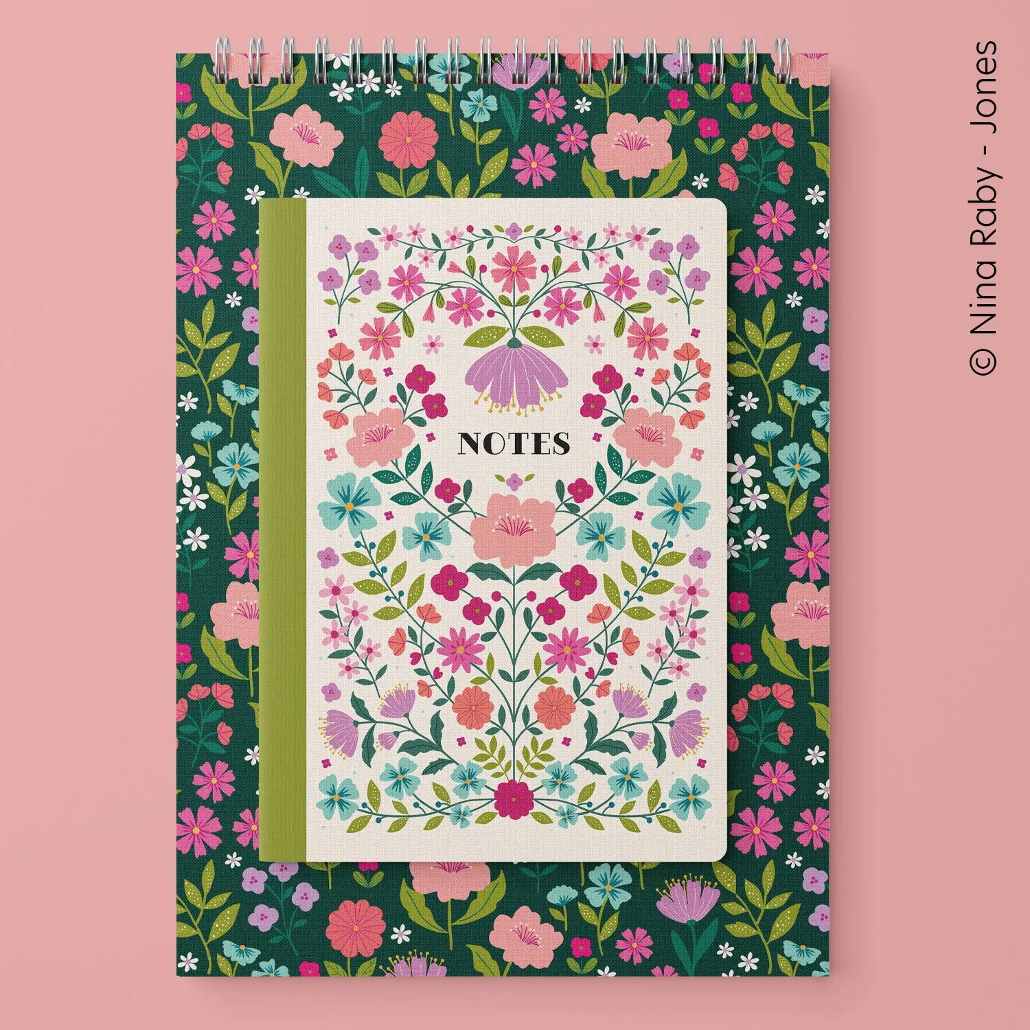 A floral patterned notebook with a white cover labeled Notes, overlaying a larger, colorful floral notebook with a spiral binding on a pink background.