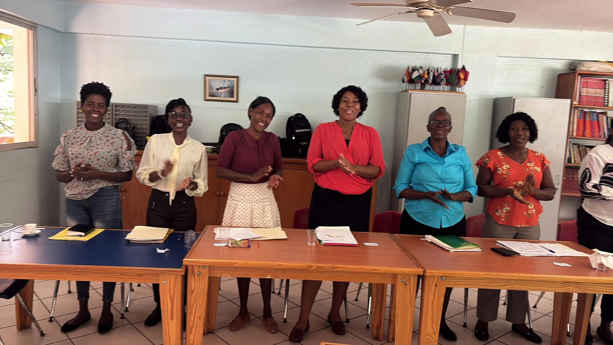Six women standing at a table clapping