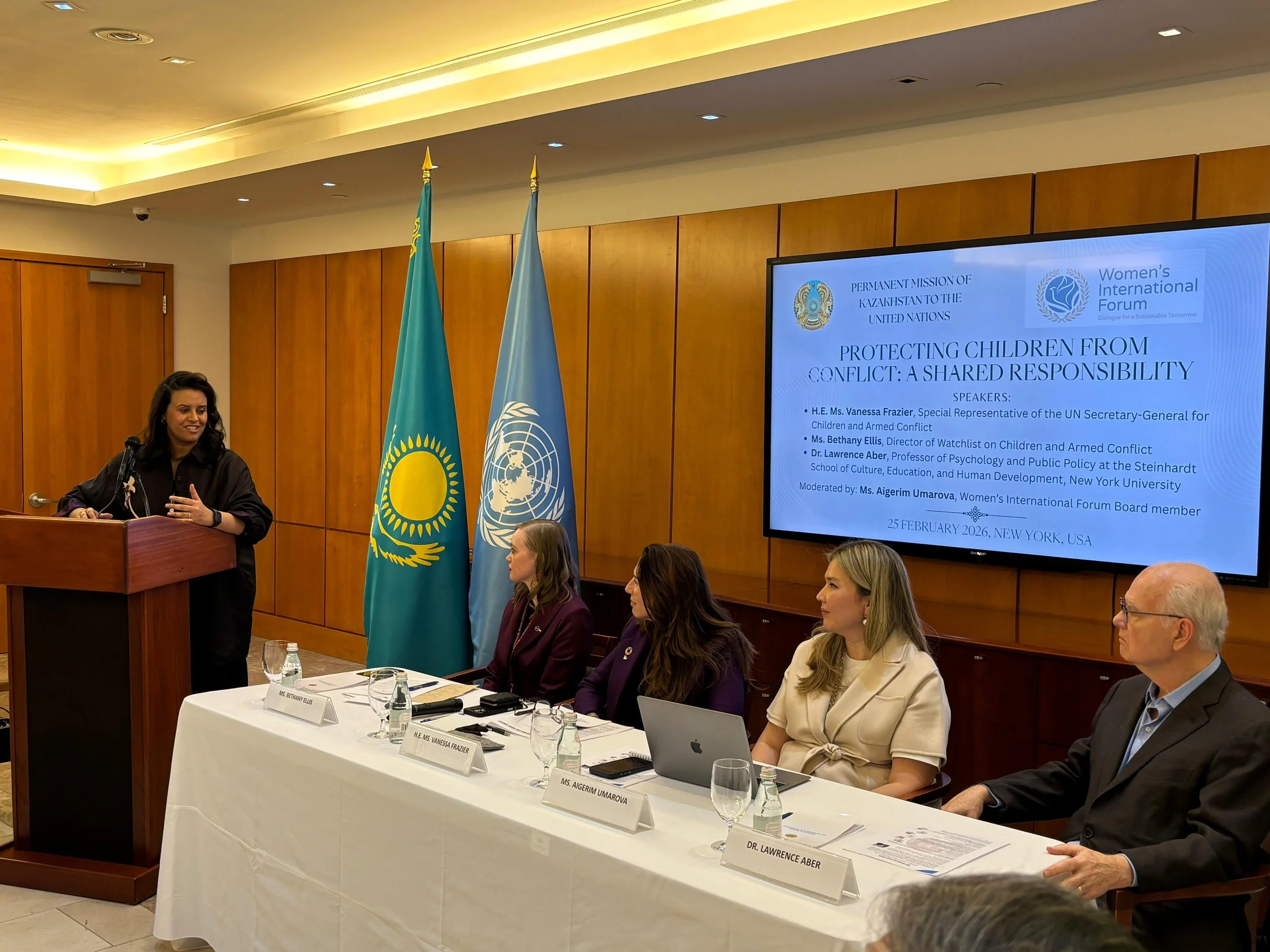 Moderator standing at a podium and four panelists seated at a table in the front of the room.