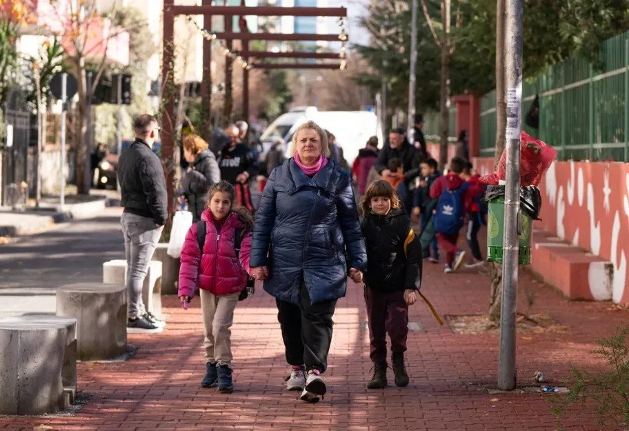 An adult caregiver walking down the street with one child on each side of her.