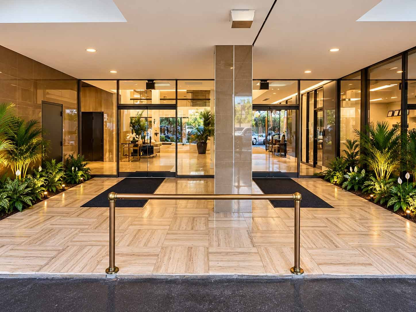 Lobby entrance of a modern building with glass doors, indoor plants, marble flooring, and seating area visible inside.