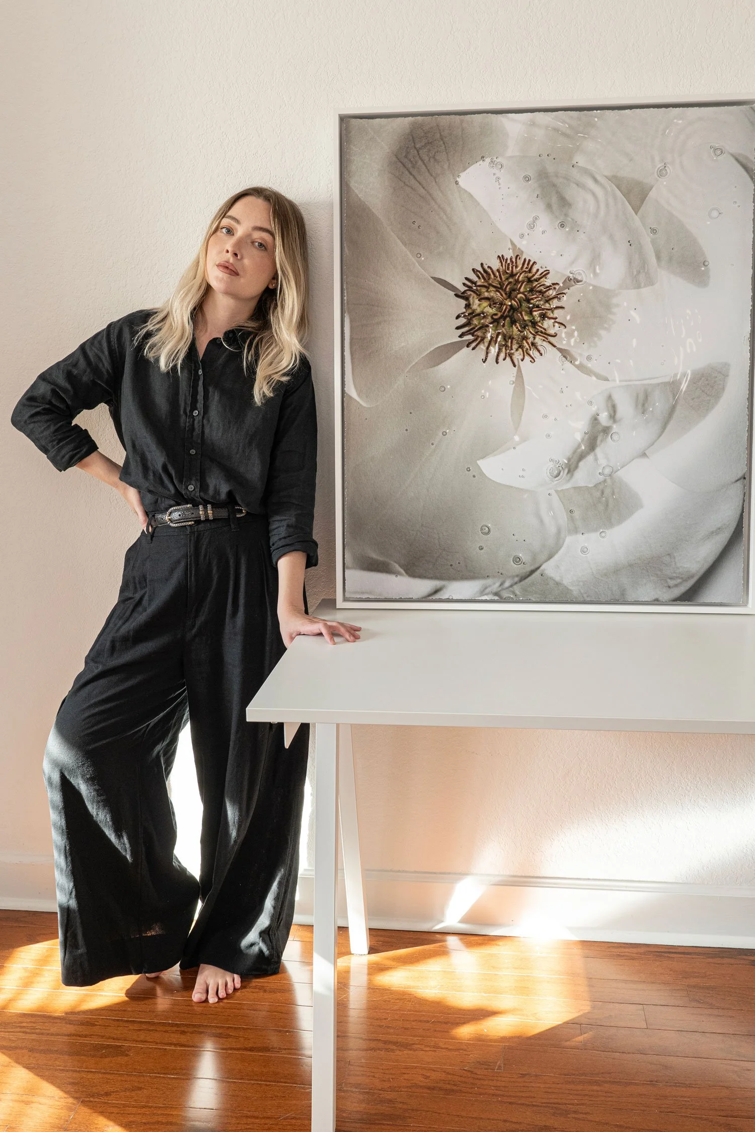 Woman in black clothing standing beside a white table and colorful botanical canvas wall art.