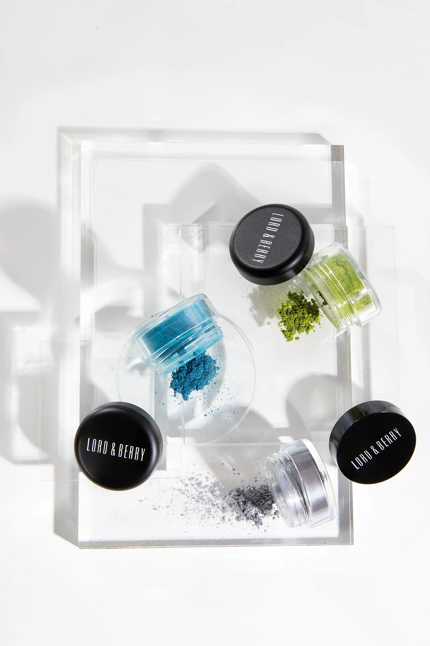 Various jars of colorful pigments, including blue, green, white, and black, displayed on a clear acrylic stand with a white background.
