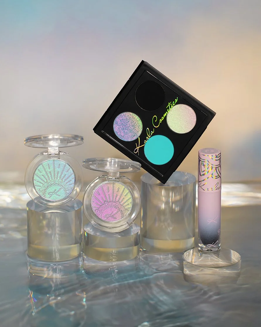 Makeup products including highlighters, a palette with pastel eyeshadows, and a lip gloss, all branded with 'Harle Coon' on a reflective surface with soft lighting.