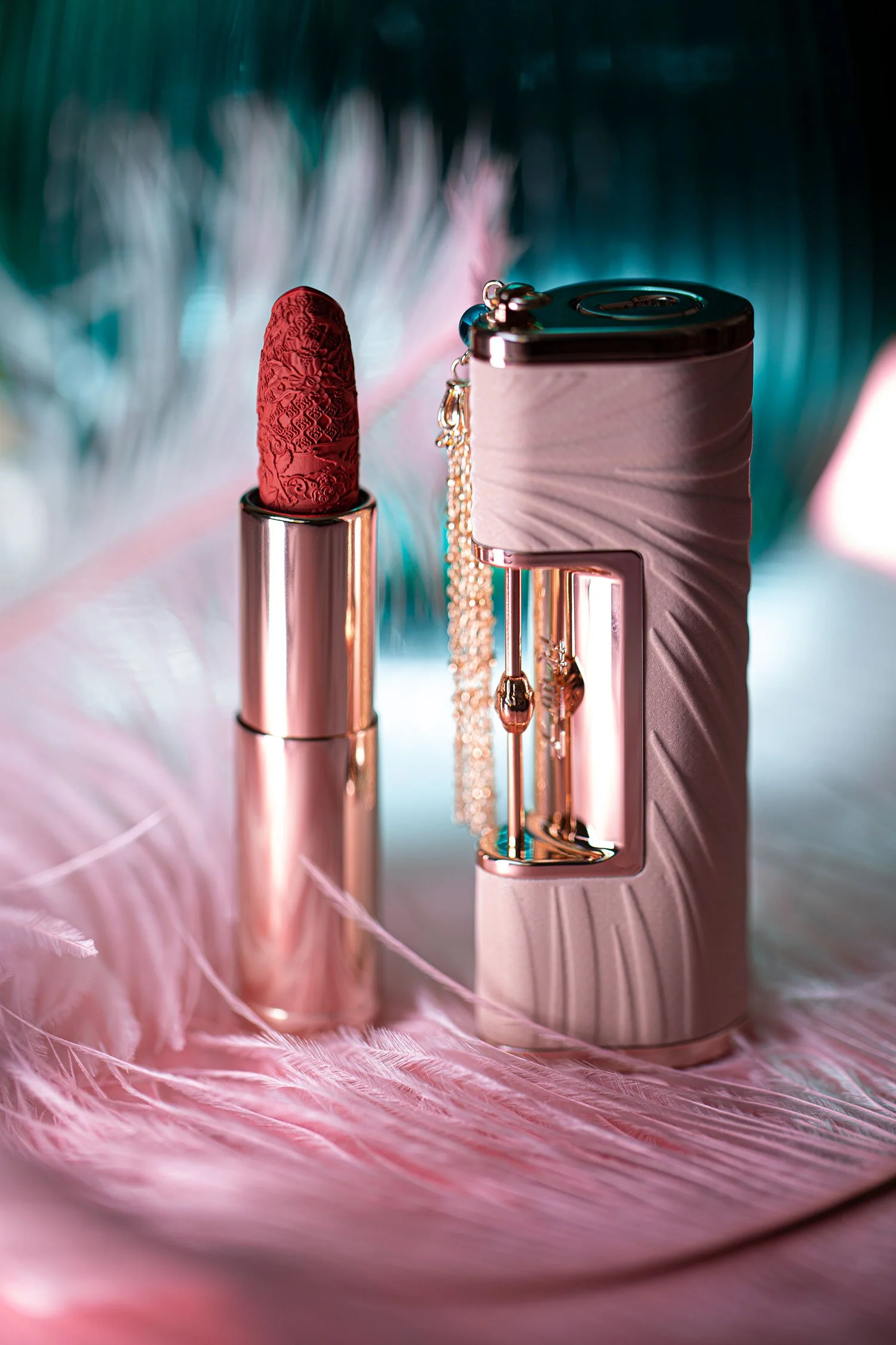A luxurious perfume bottle and a lipstick with intricate designs on a soft pink feather background.