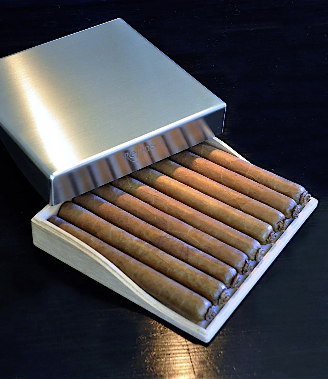 A wooden box with a metal lid holding several cigars.