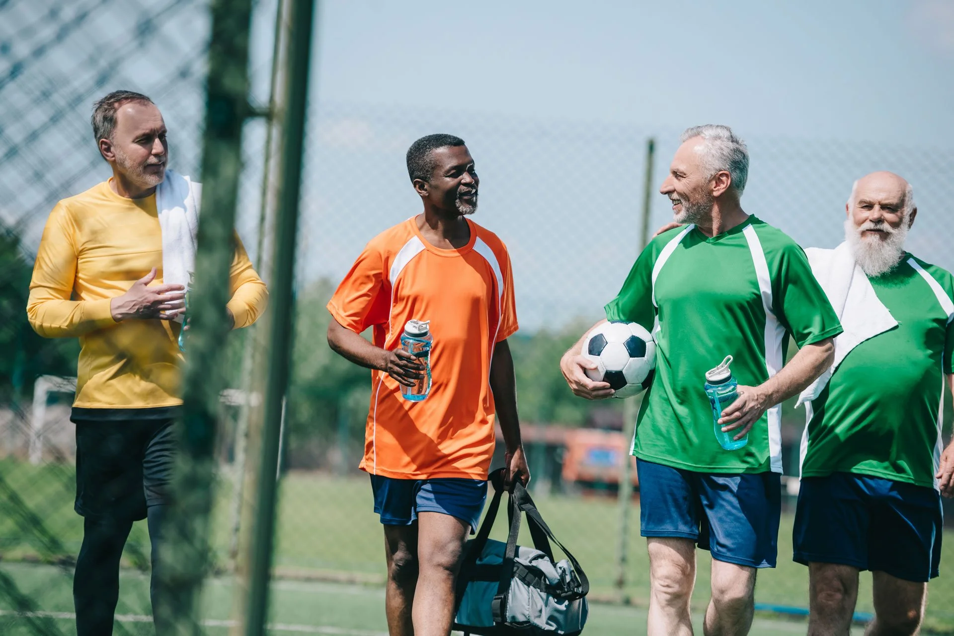photo of four elderly men smiling walking off a football pitch with equipment in their arms.