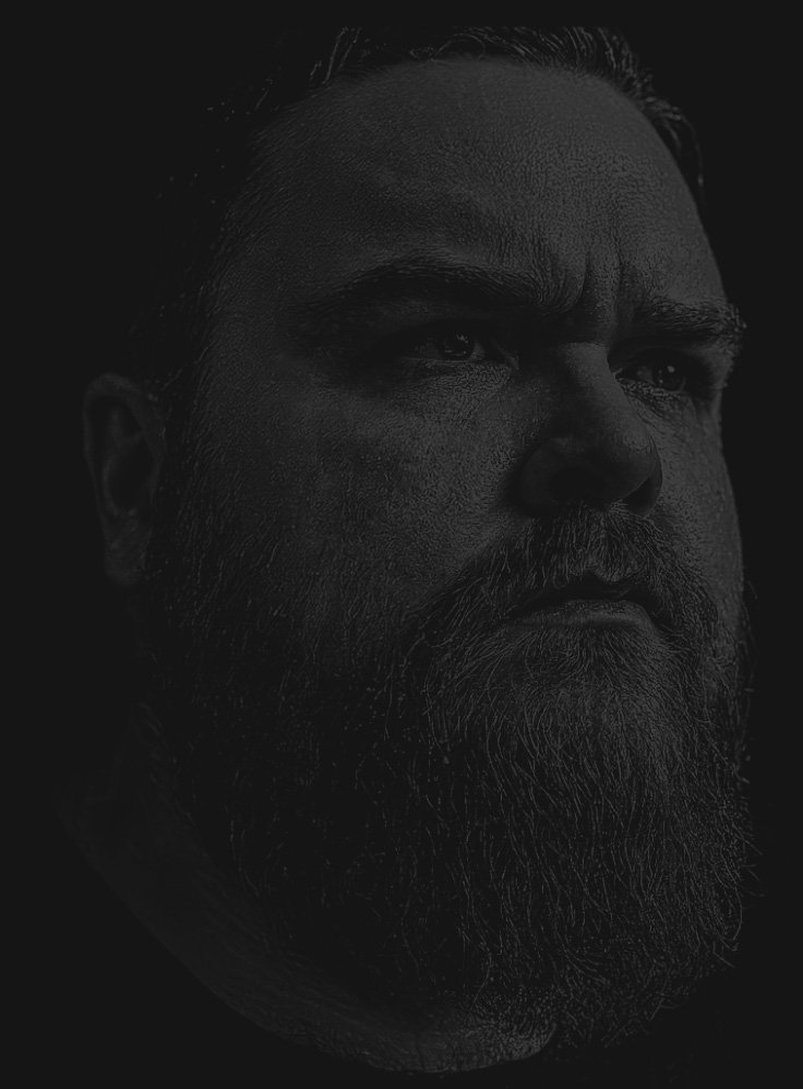 Close-up black and white portrait of a man with a beard and serious expression.