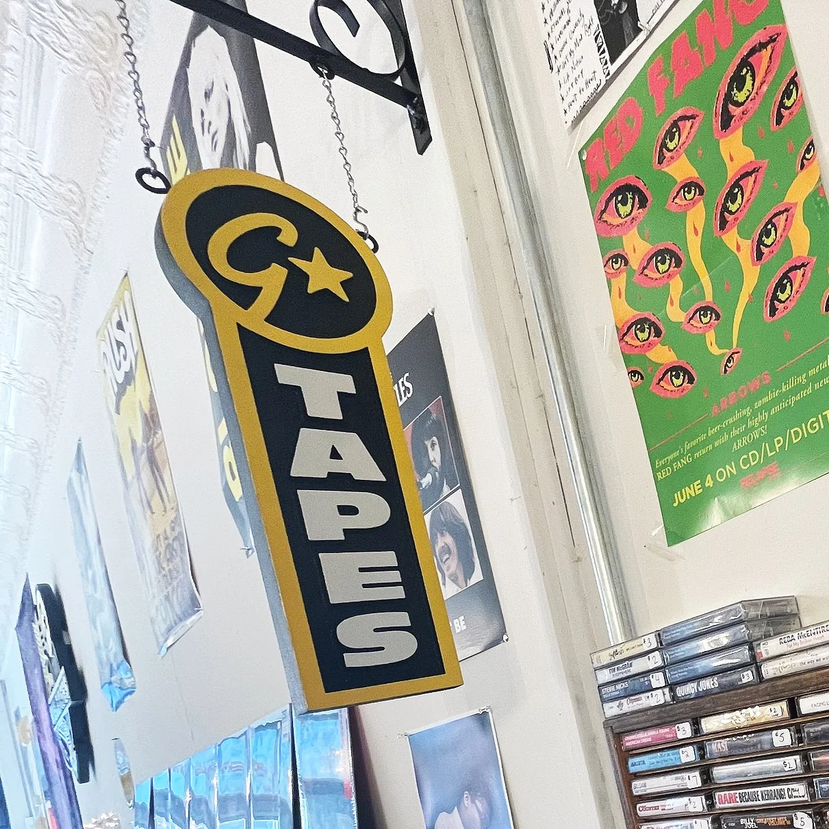 Sign with the word 'CATASTROPHES' on a yellow and black background, featuring several painted eyes on a green background, and a collection of CDs or DVDs below.