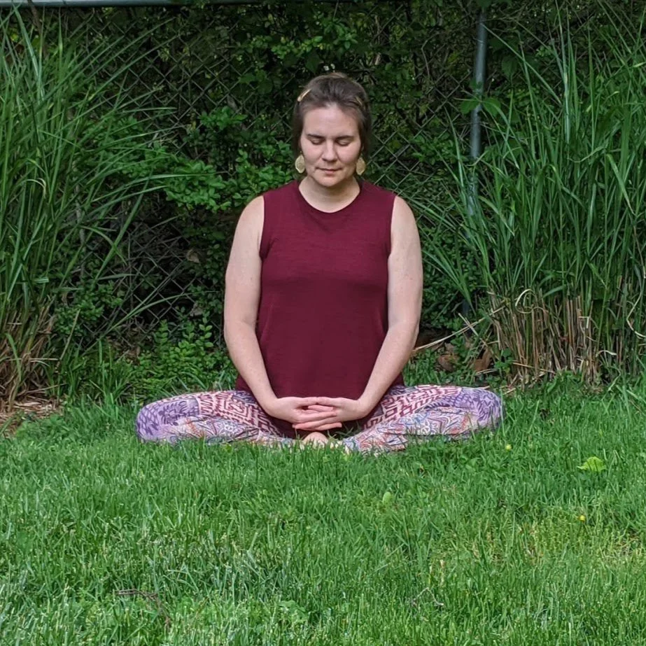 alt= "women meditating outside in the grass"