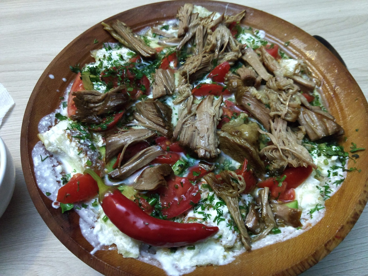Qurutob, the pride and “national dish,” of the Tajiks. Layered unleavened bread and sour yogurt, tender stewed lamb, fresh greens, onion, and hot peppers, served in a shallow wooden bowl. Qurutob comes in many regional varieties.