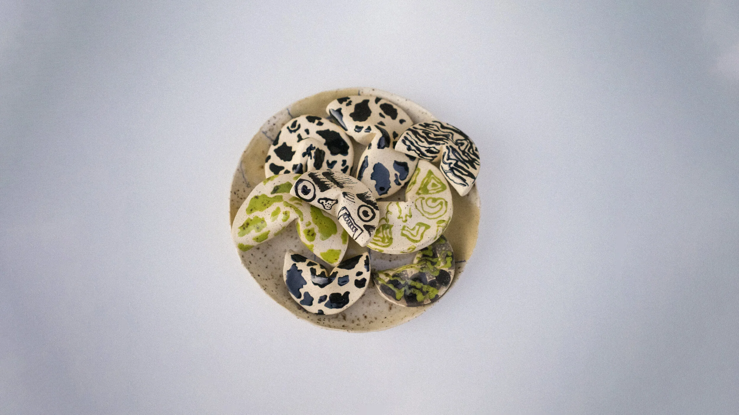 Assorted cow-shaped and oval-shaped decorative stones with abstract black, white, green, and blue patterns on a round ceramic plate.
