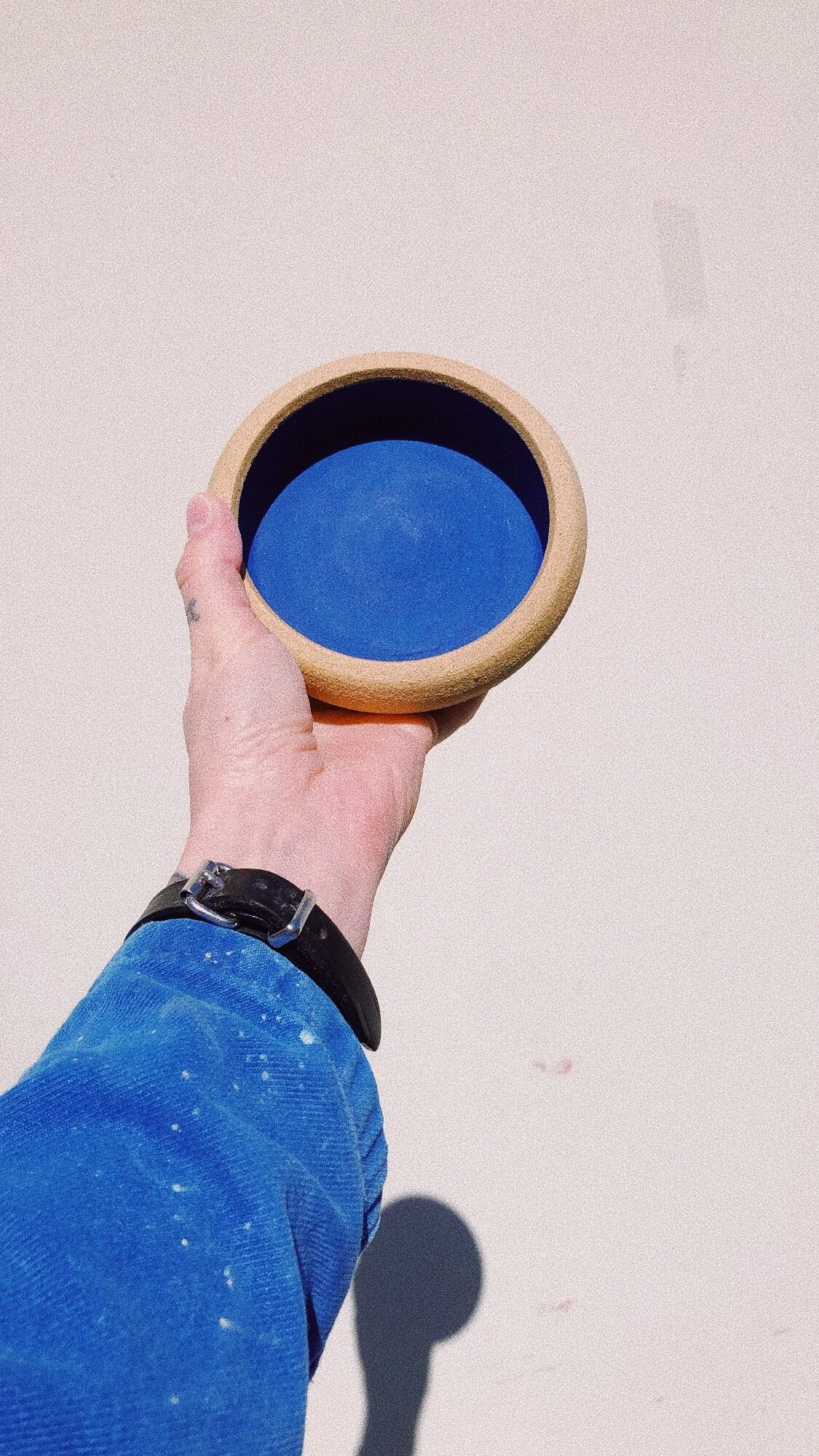 A person's hand holding a circular object with an outer beige rim and a blue inner surface, against a plain light background.