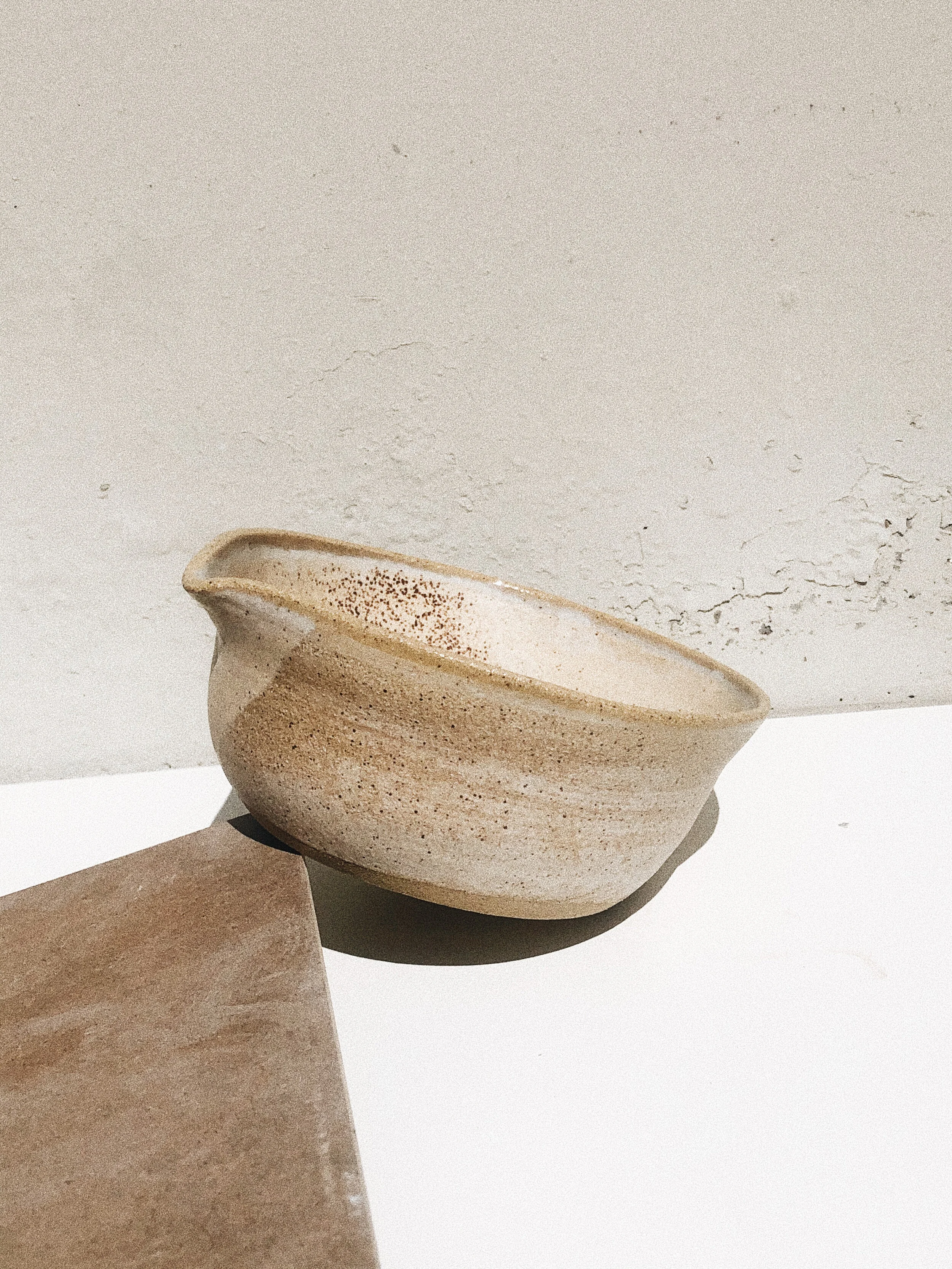 A cream-colored ceramic bowl with a speckled pattern, placed on a white surface with a shadow cast underneath.