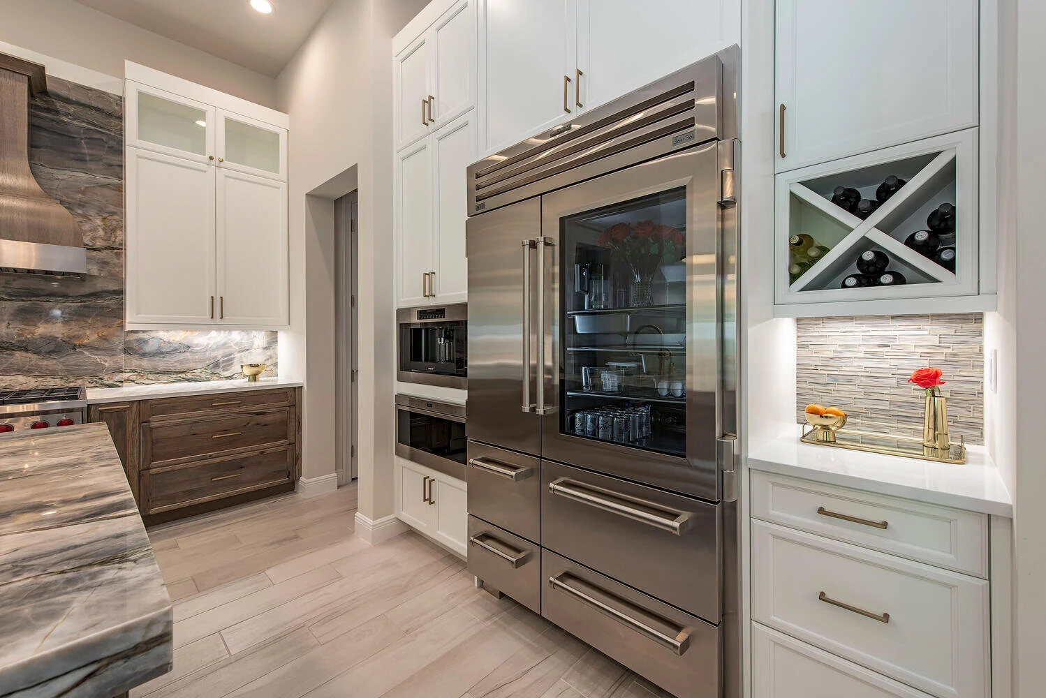 Modern kitchen with white cabinetry, a stainless steel double oven and a wine rack, marble countertops, and a glass-front refrigerator.