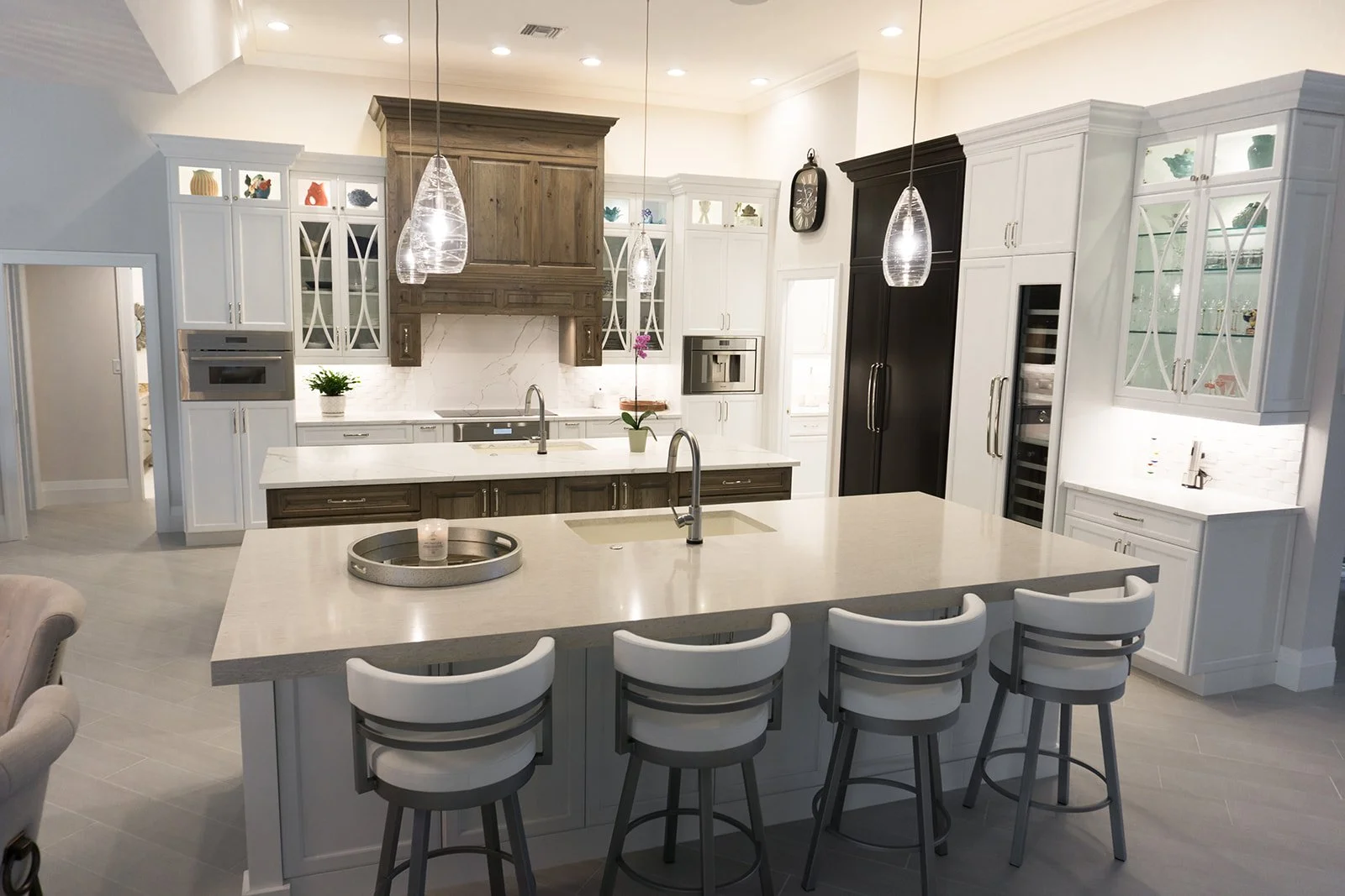 Modern kitchen with white and dark wood cabinetry, white marble backsplash, island with bar seating, pendant lighting, and built-in appliances.