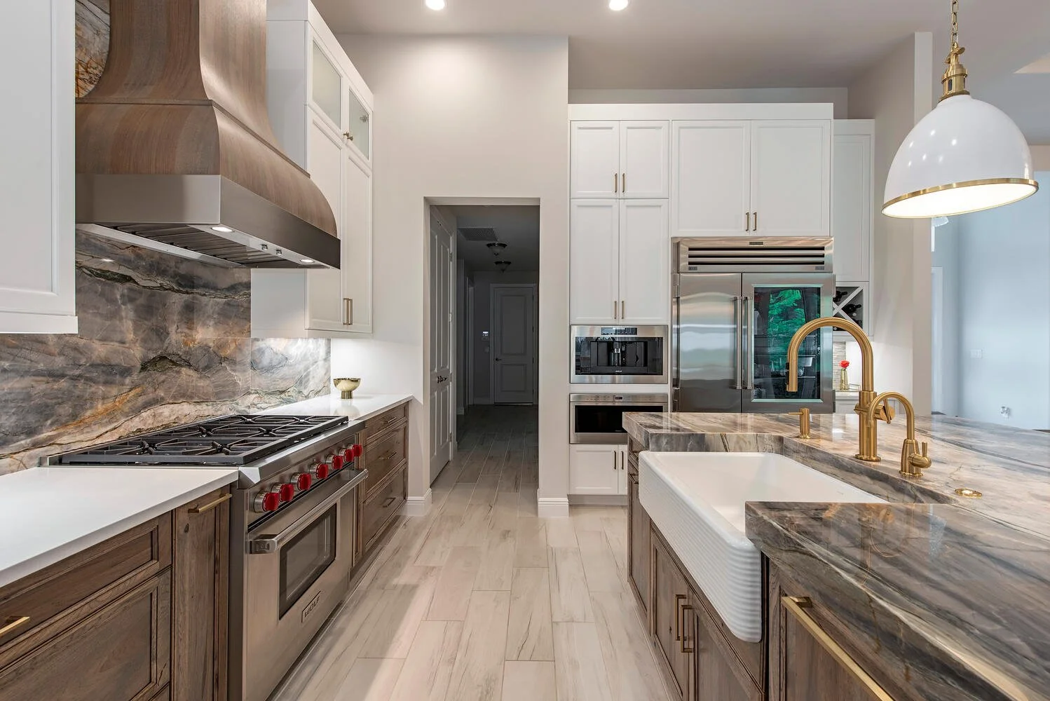 Modern kitchen with white upper cabinets, wooden lower cabinets, gray marble backsplash, stainless steel appliances, and a large granite countertop with gold fixtures.
