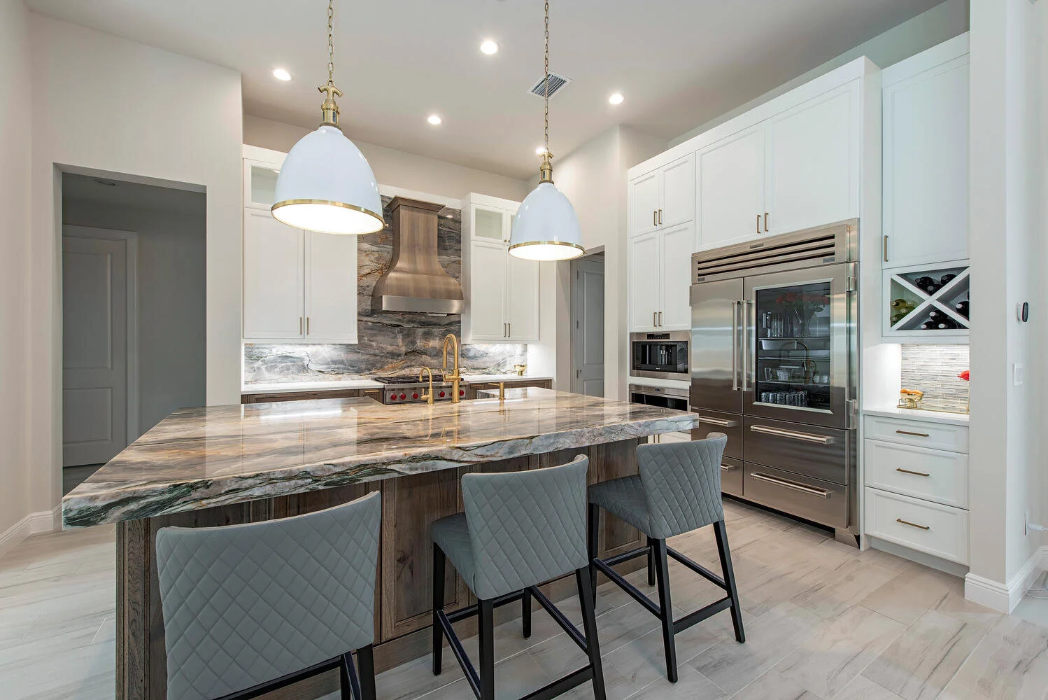Modern kitchen with white cabinets, marble countertop island, stainless steel appliances, and two pendant lights.