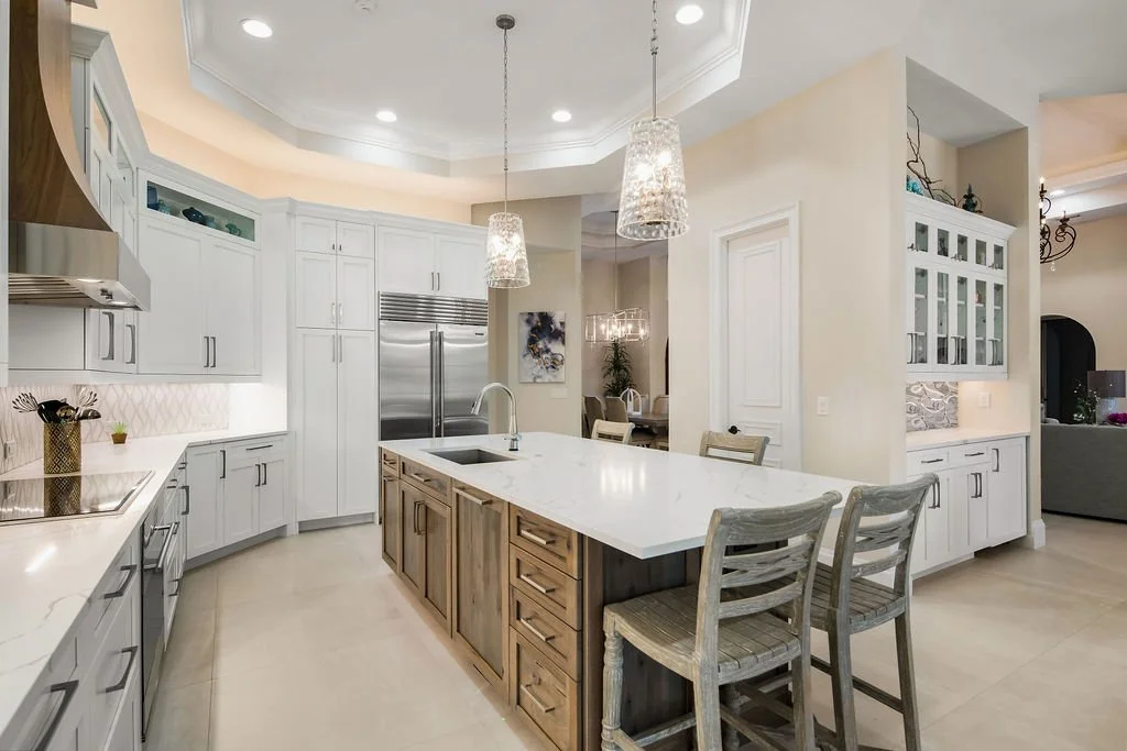 Bright modern kitchen with white cabinets, a large island with wooden base, pendant lighting, and stainless steel appliances.
