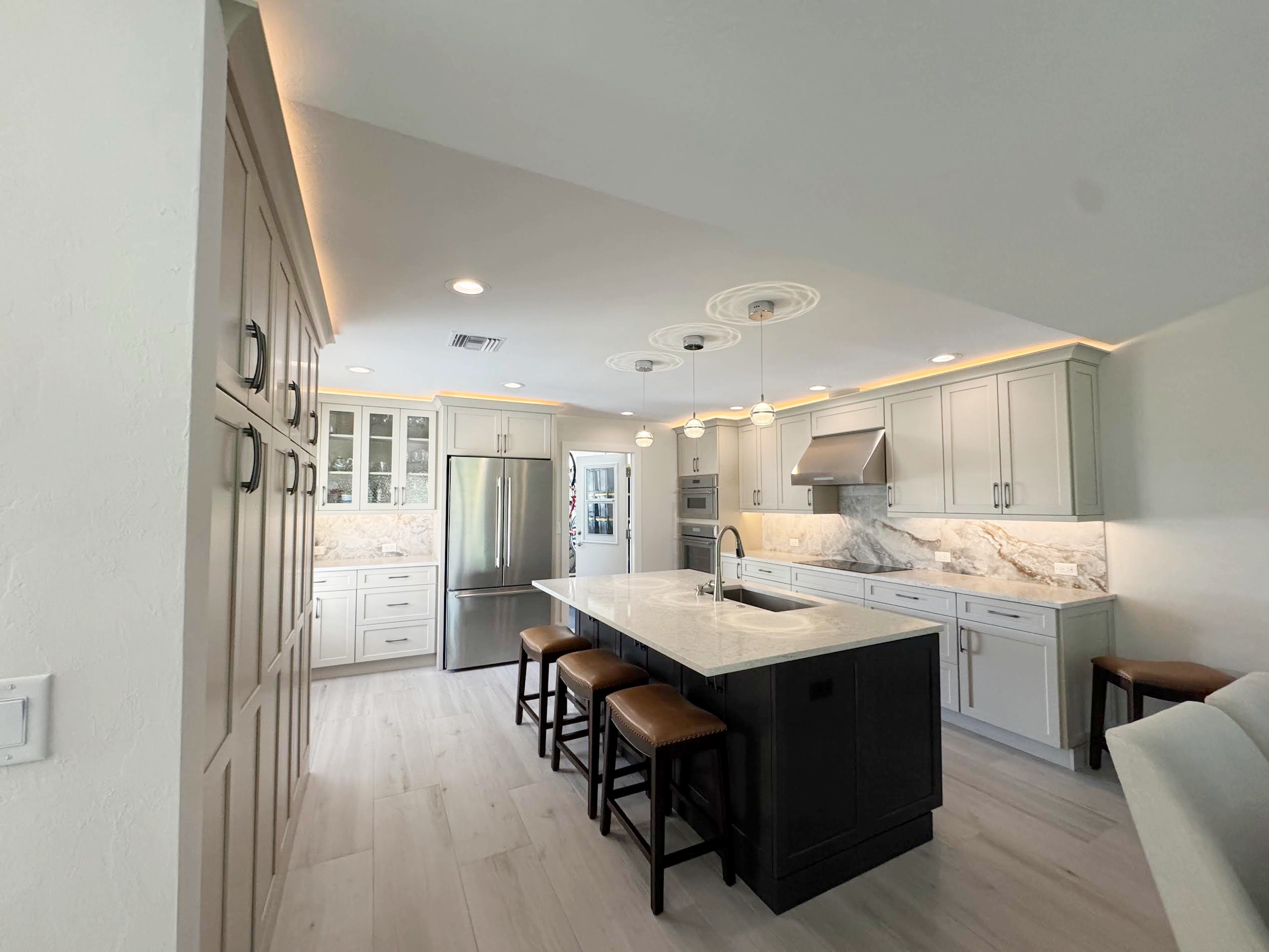 Modern kitchen with white cabinets, a large center island, stainless steel appliances, pendant lights over the island, a marble backsplash, and a breakfast bar with four stools.