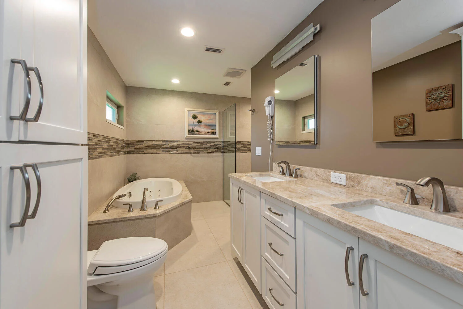 Bathroom with dual sinks, a bathtub with jets, a shower area, and tropical artwork on the wall.