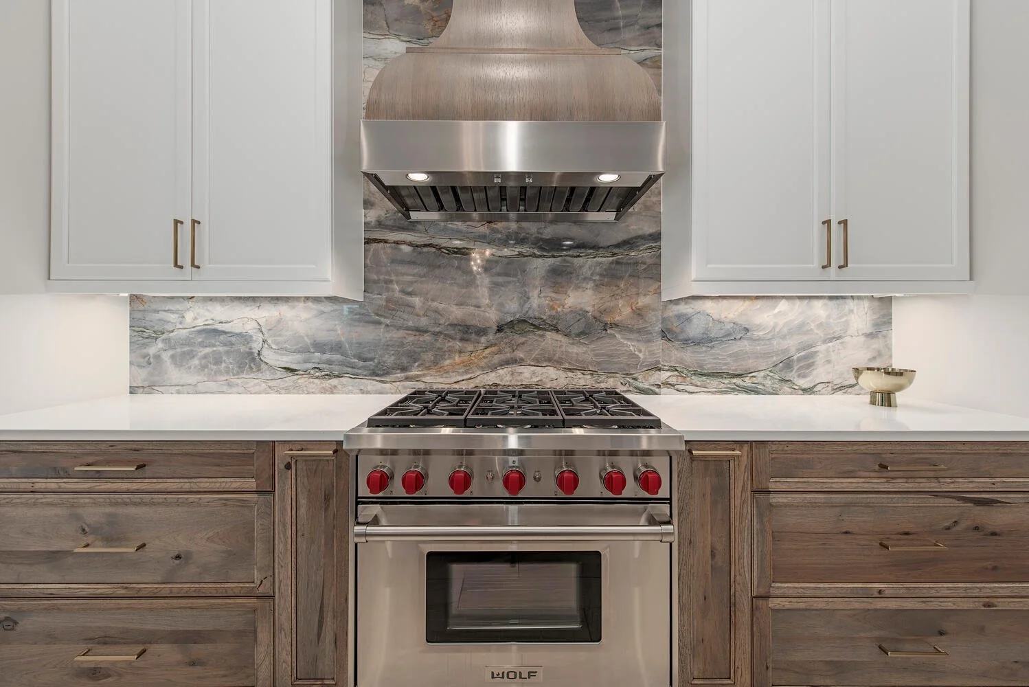 Modern kitchen with a stainless steel Wolf oven, gray marble backsplash, white upper cabinets, and wood lower cabinets.