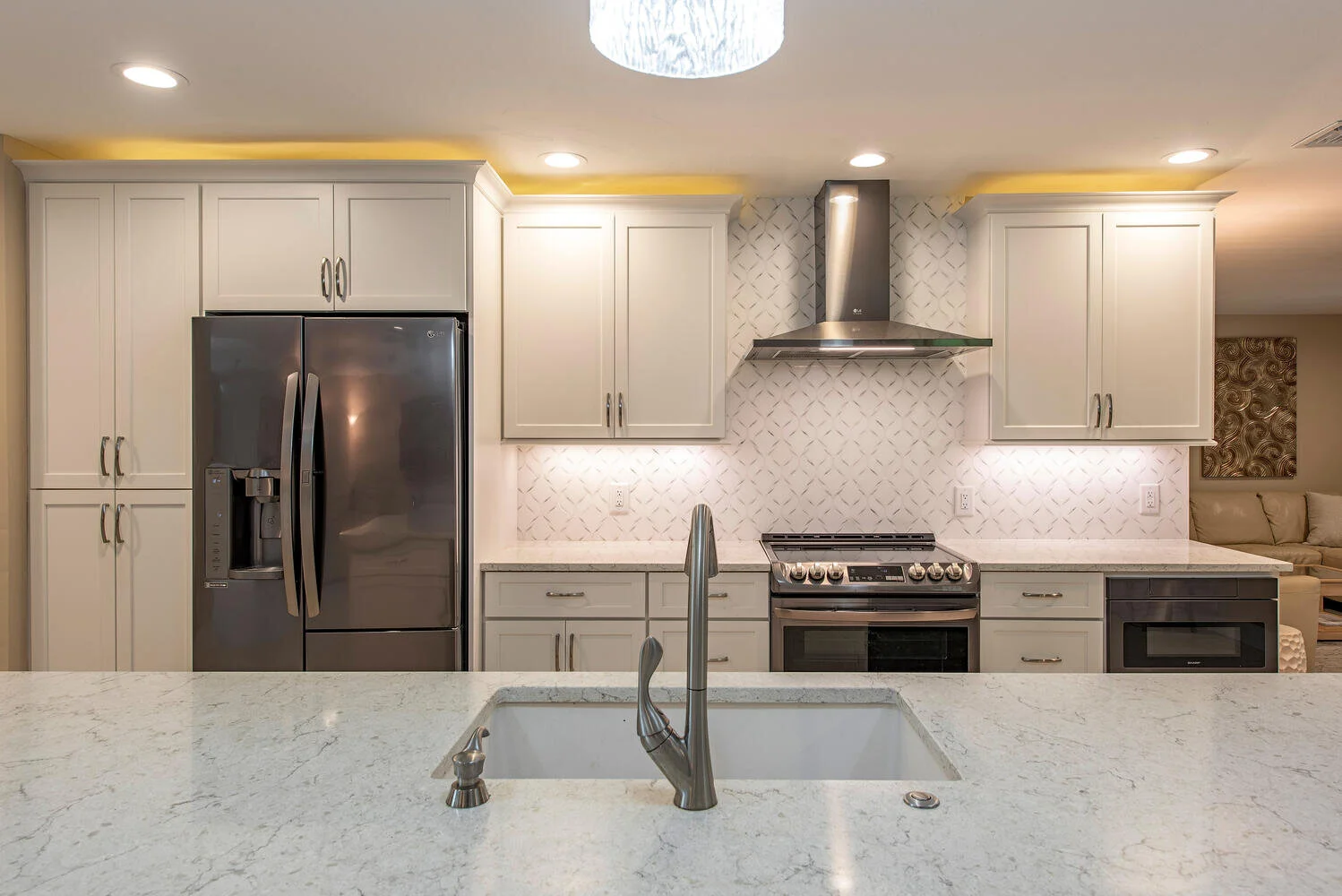 Modern kitchen with white cabinets, stainless steel refrigerator, stove, microwave, and a marble countertop island with a sink and faucet.