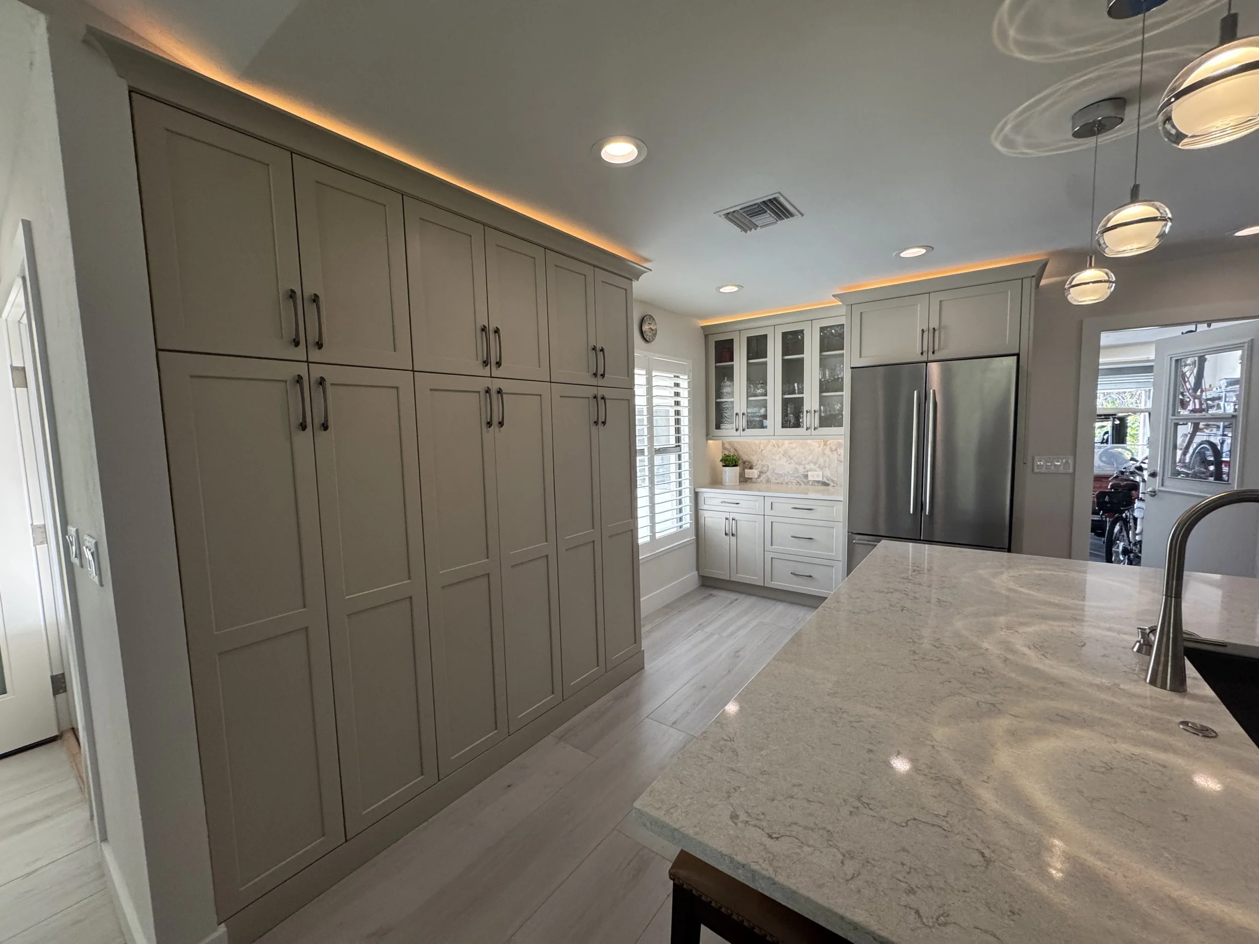 Modern kitchen with beige cabinets, a refrigerator, white marble countertops, ceiling lighting, and windows with white blinds.