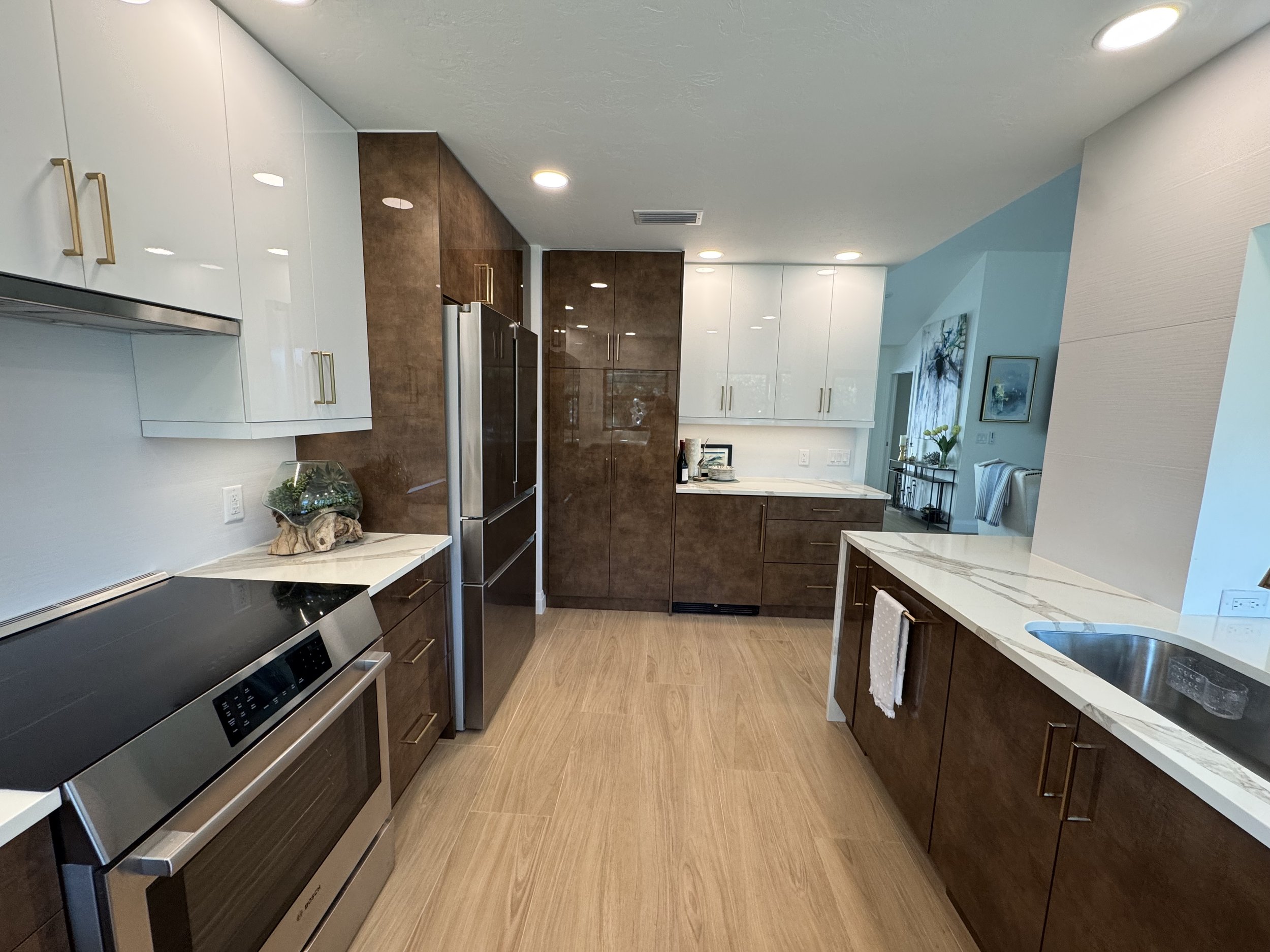 Modern kitchen with white and brown cabinets, stainless steel appliances, a marble countertop, and recessed ceiling lights.