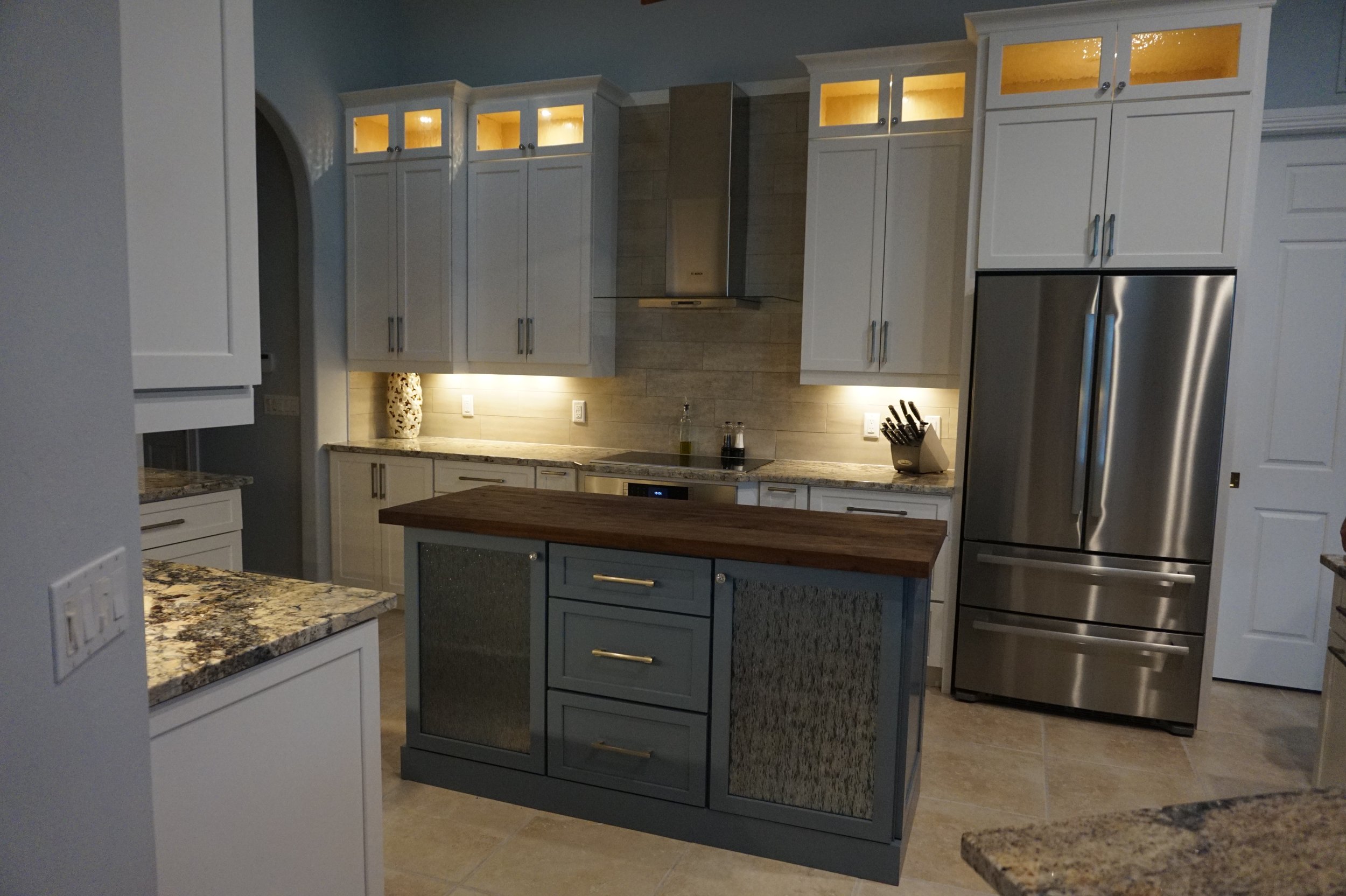 Modern kitchen with white cabinets, granite countertops, stainless steel refrigerator, wood and tile flooring, and recessed lighting.
