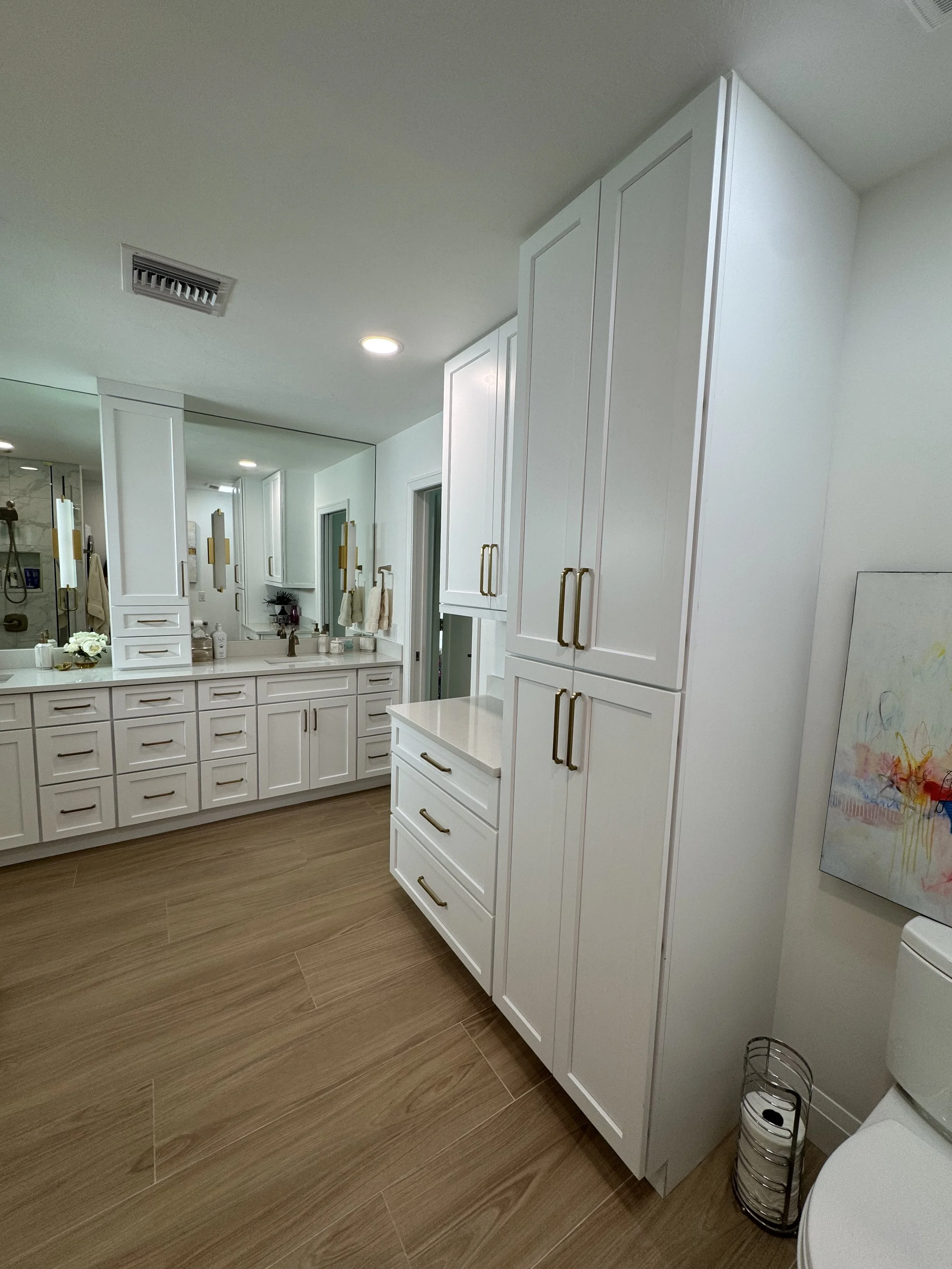 Modern bathroom with white cabinetry, a large mirror, and wooden flooring.