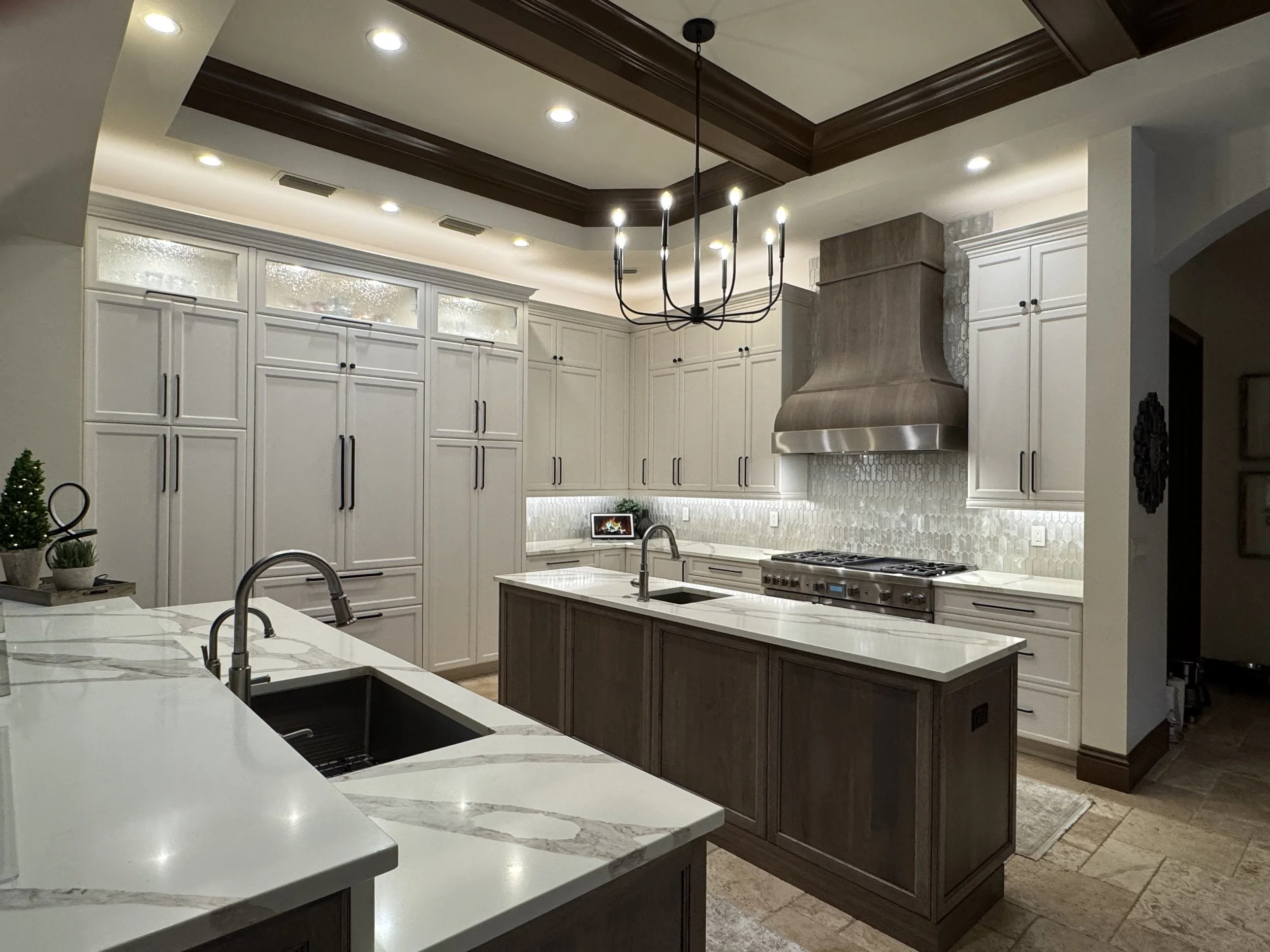 Modern kitchen with white cabinets, a large kitchen island with a marble countertop, a hanging chandelier, built-in appliances, and recessed lighting.