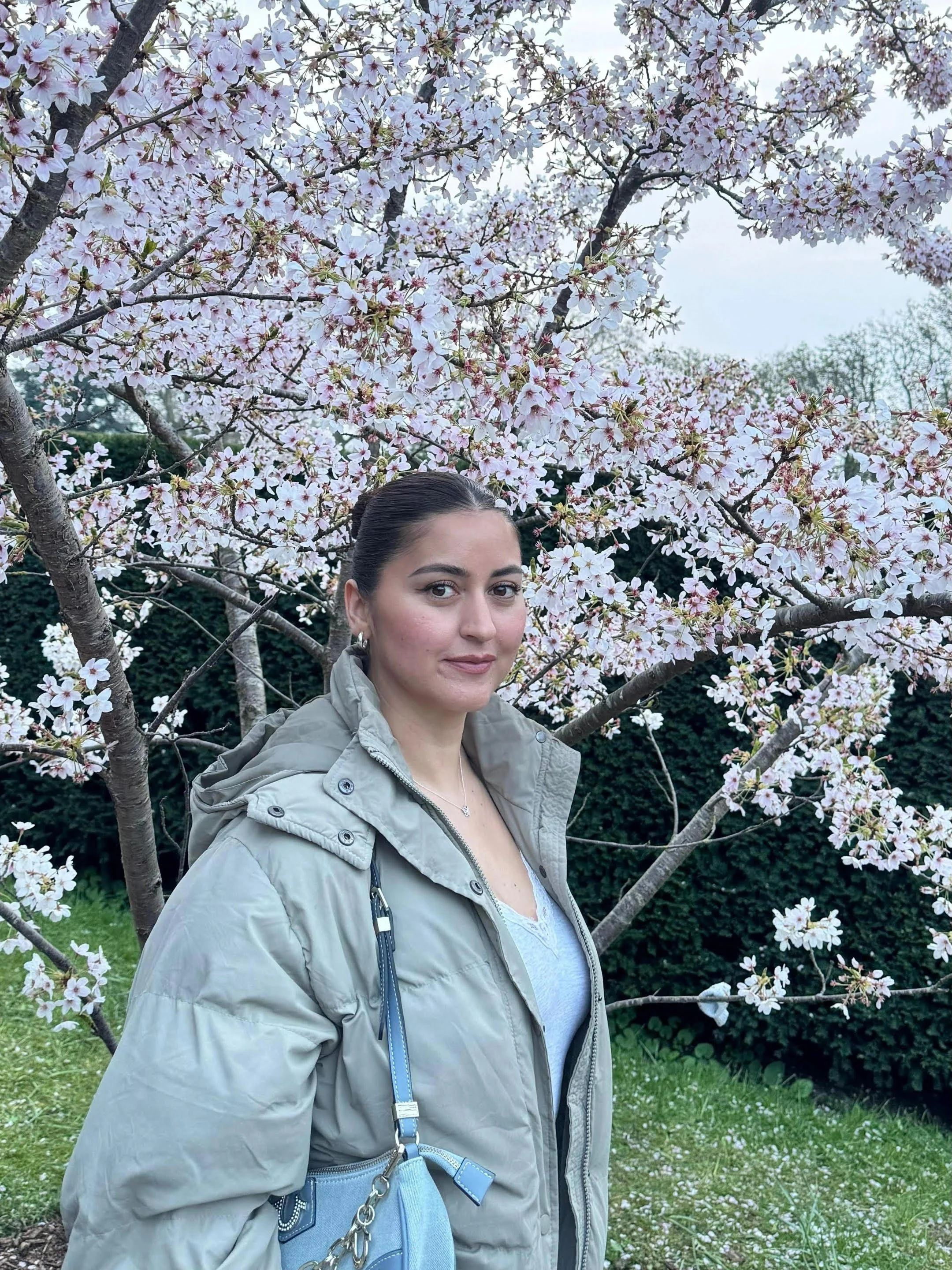 A young woman in a pink jacket kneeling among pink tulips in a flower field on a sunny day.