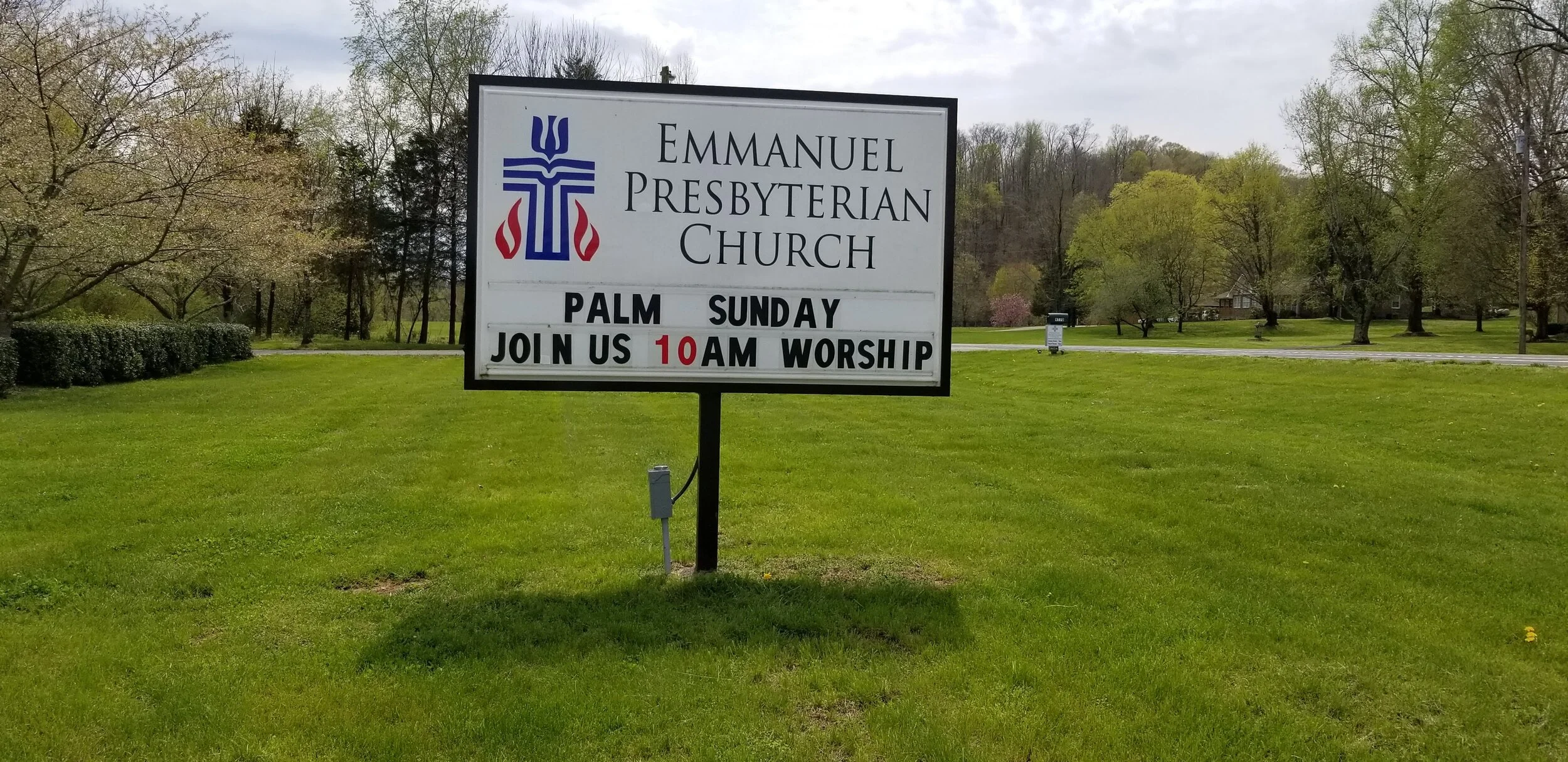 Sign for Emmanuel Presbyterian Church, announcing Palm Sunday service at 10 AM, surrounded by grass and trees.
