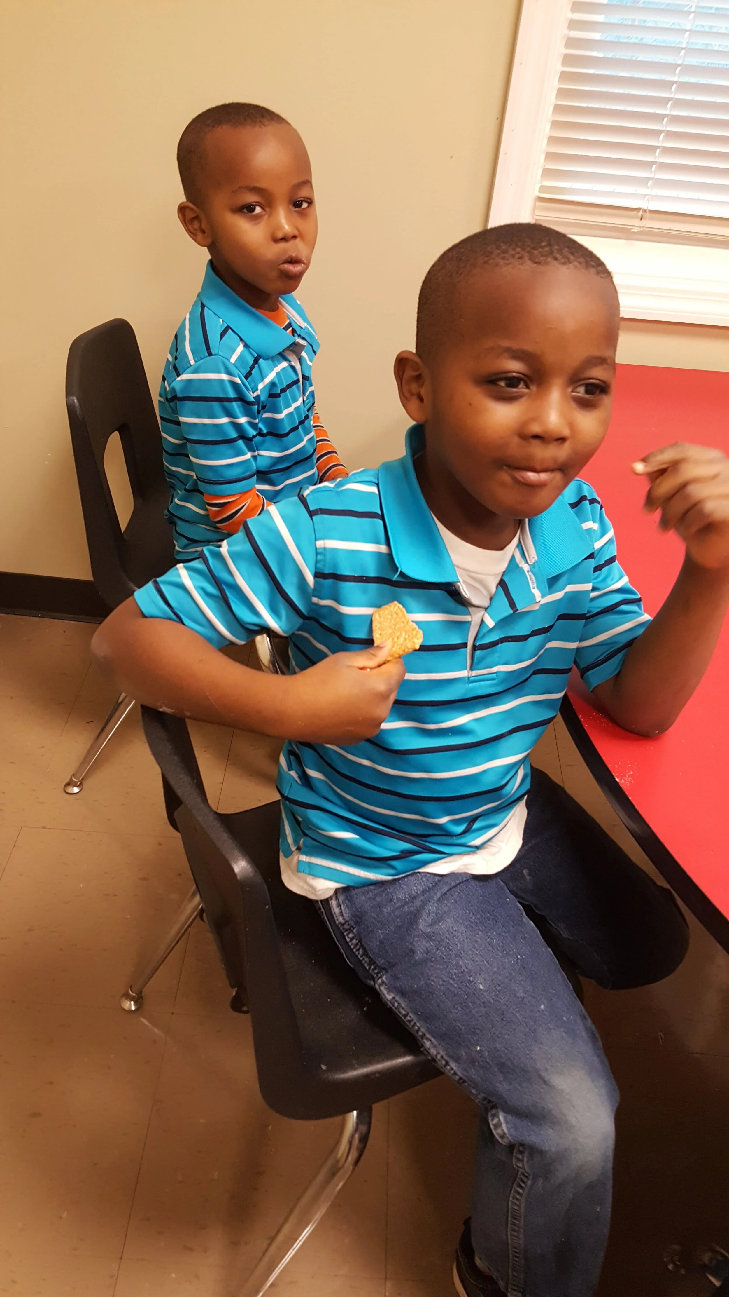 Two boys in striped shirts sitting at a table with one holding a cracker.