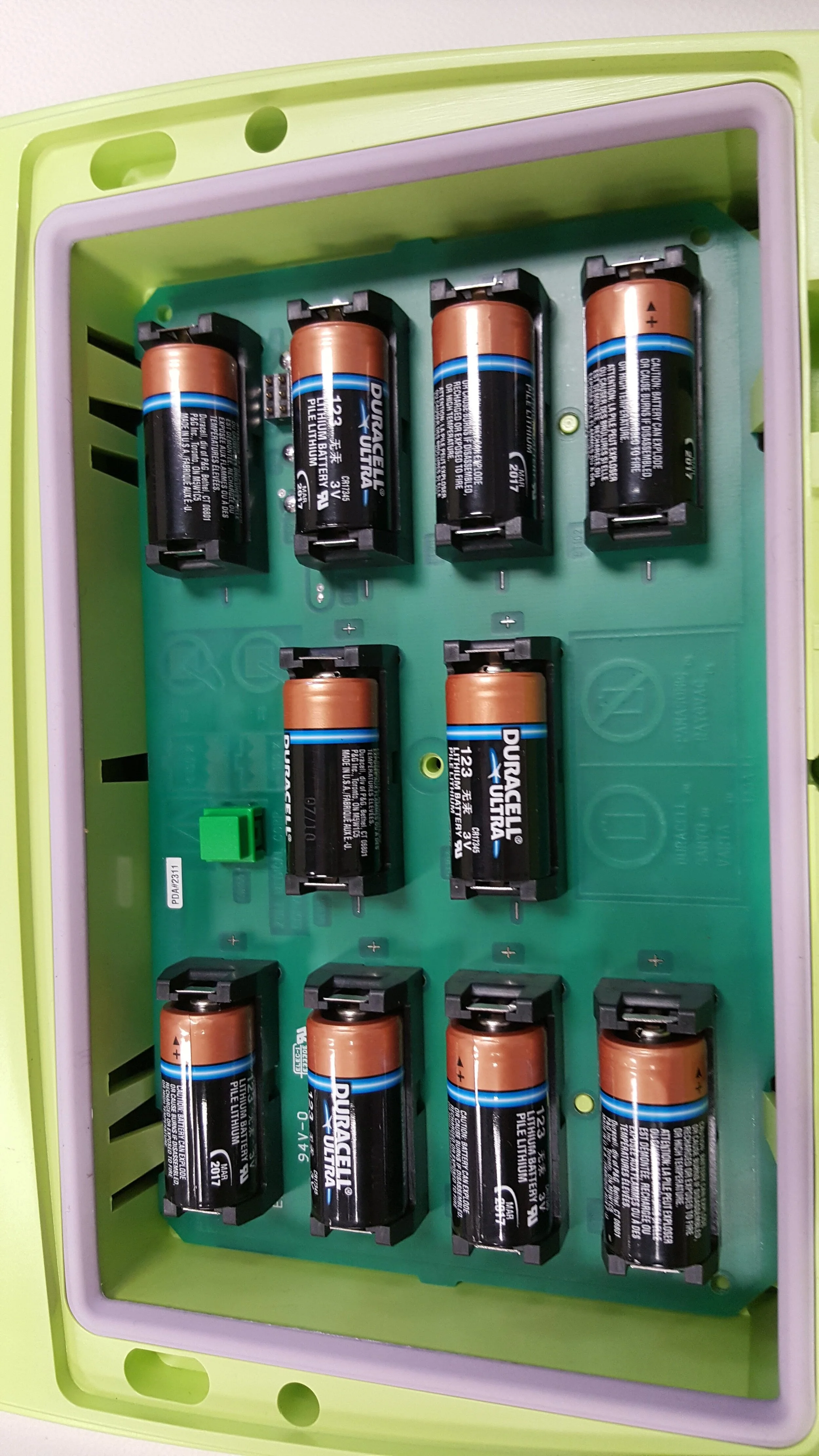 A green electronic device housing with ten installed Duracell Ultra 123 3V lithium batteries, arranged in two rows on a circuit board.