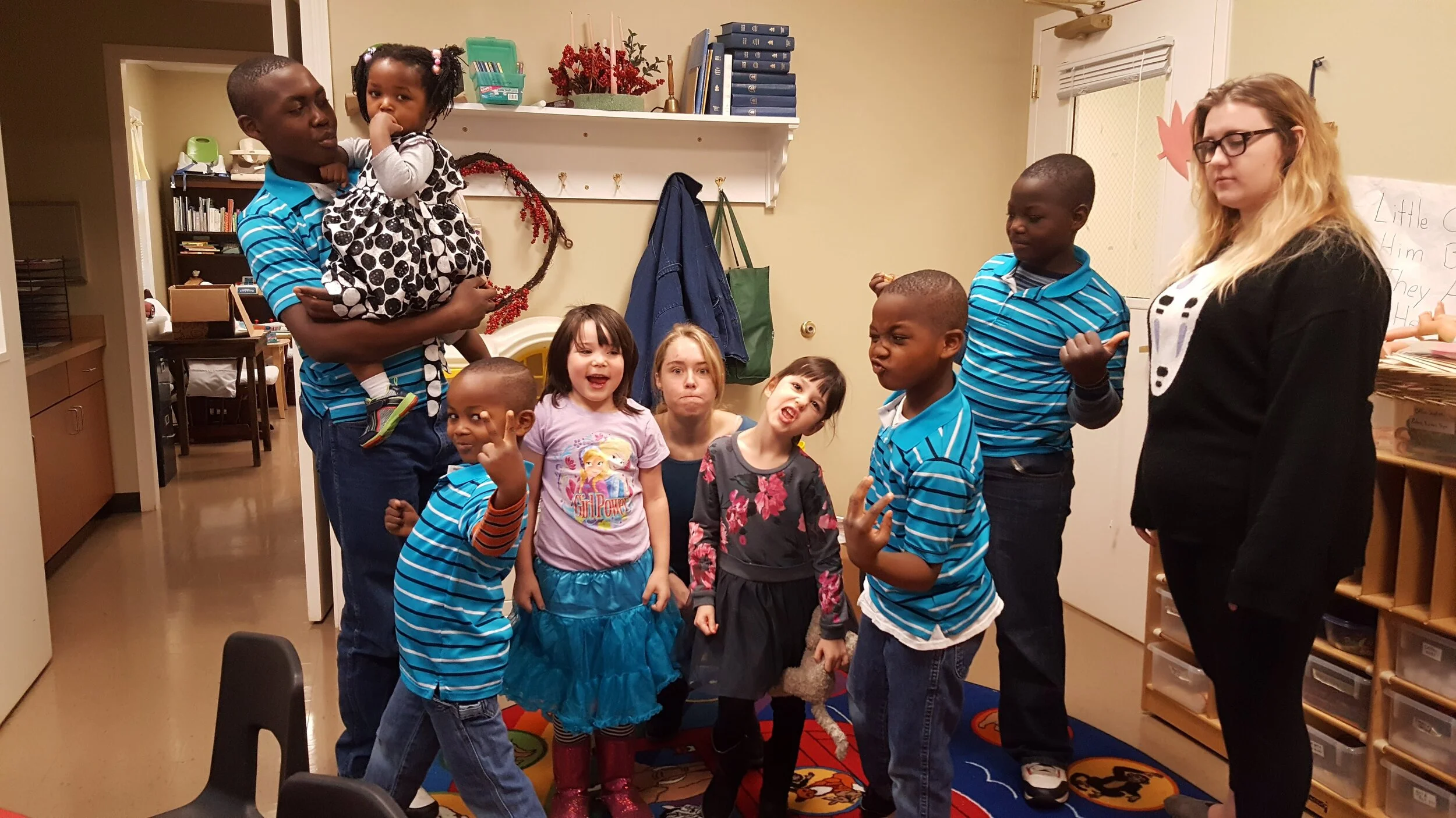 Group of children and adults in a classroom posing playfully.