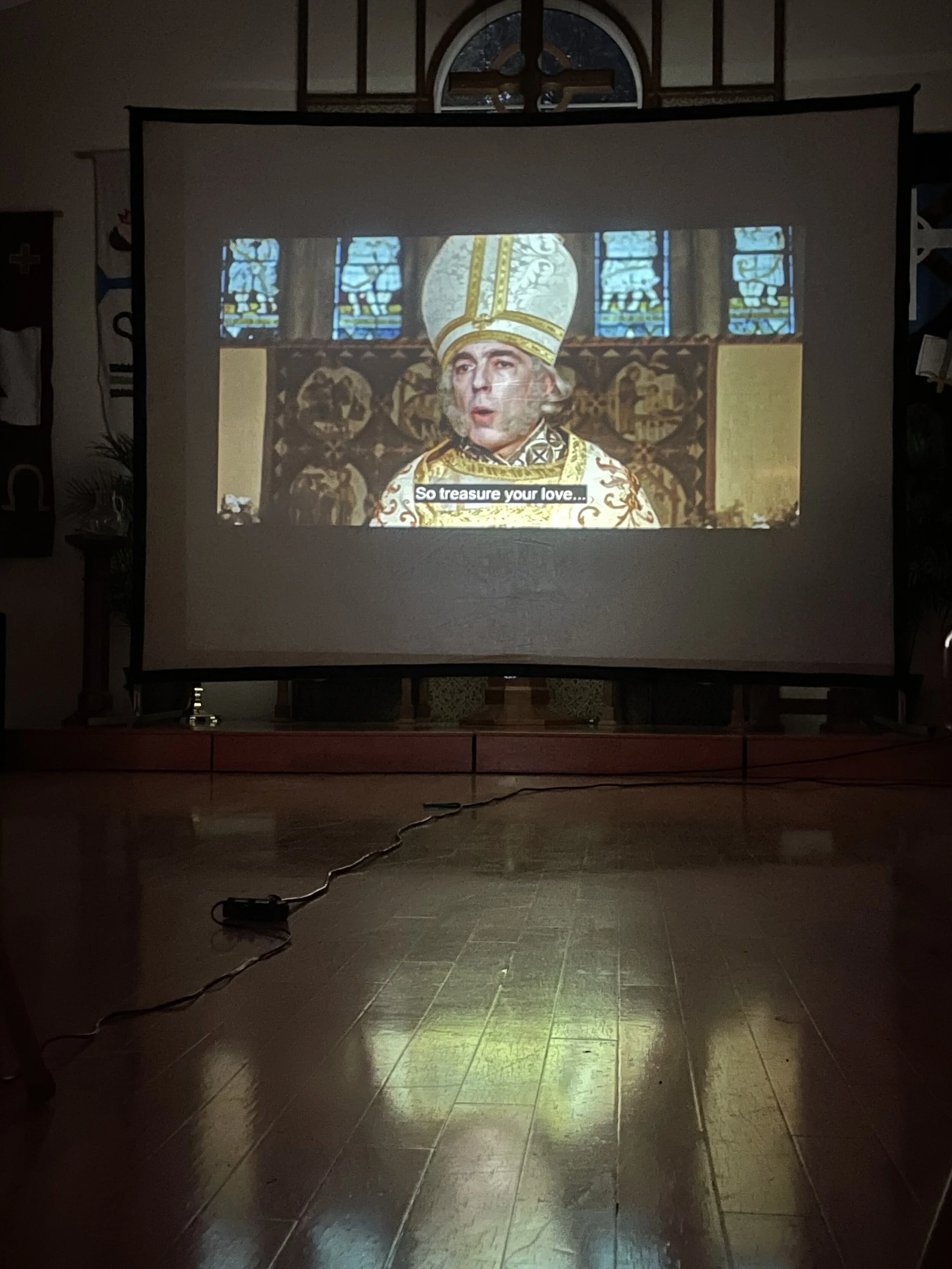 Scene projected on screen showing a character in ornate religious attire with subtitle "So treasure your love..."