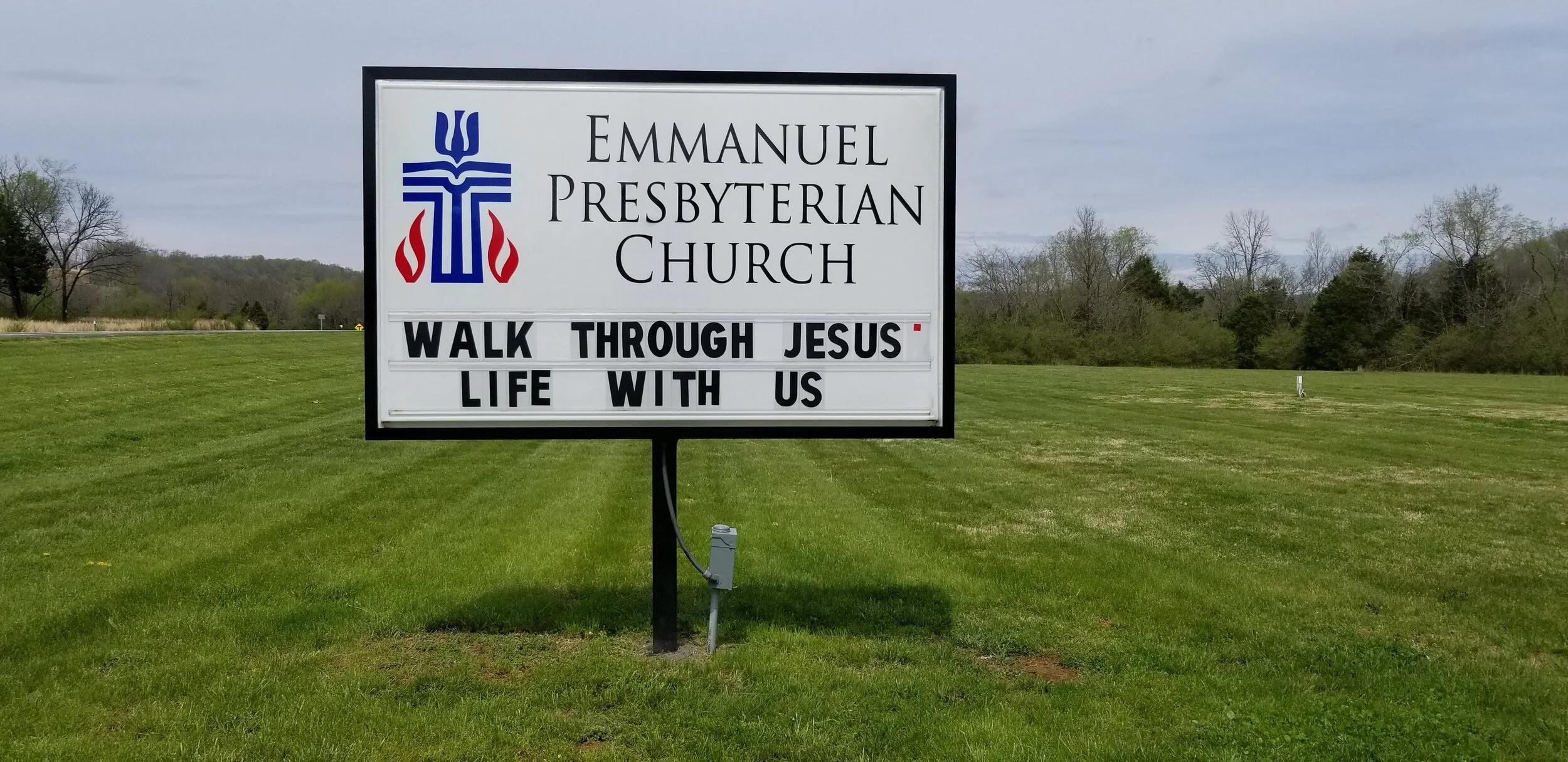 Sign for Emmanuel Presbyterian Church with message "Walk Through Jesus' Life With Us" on a grassy lawn.
