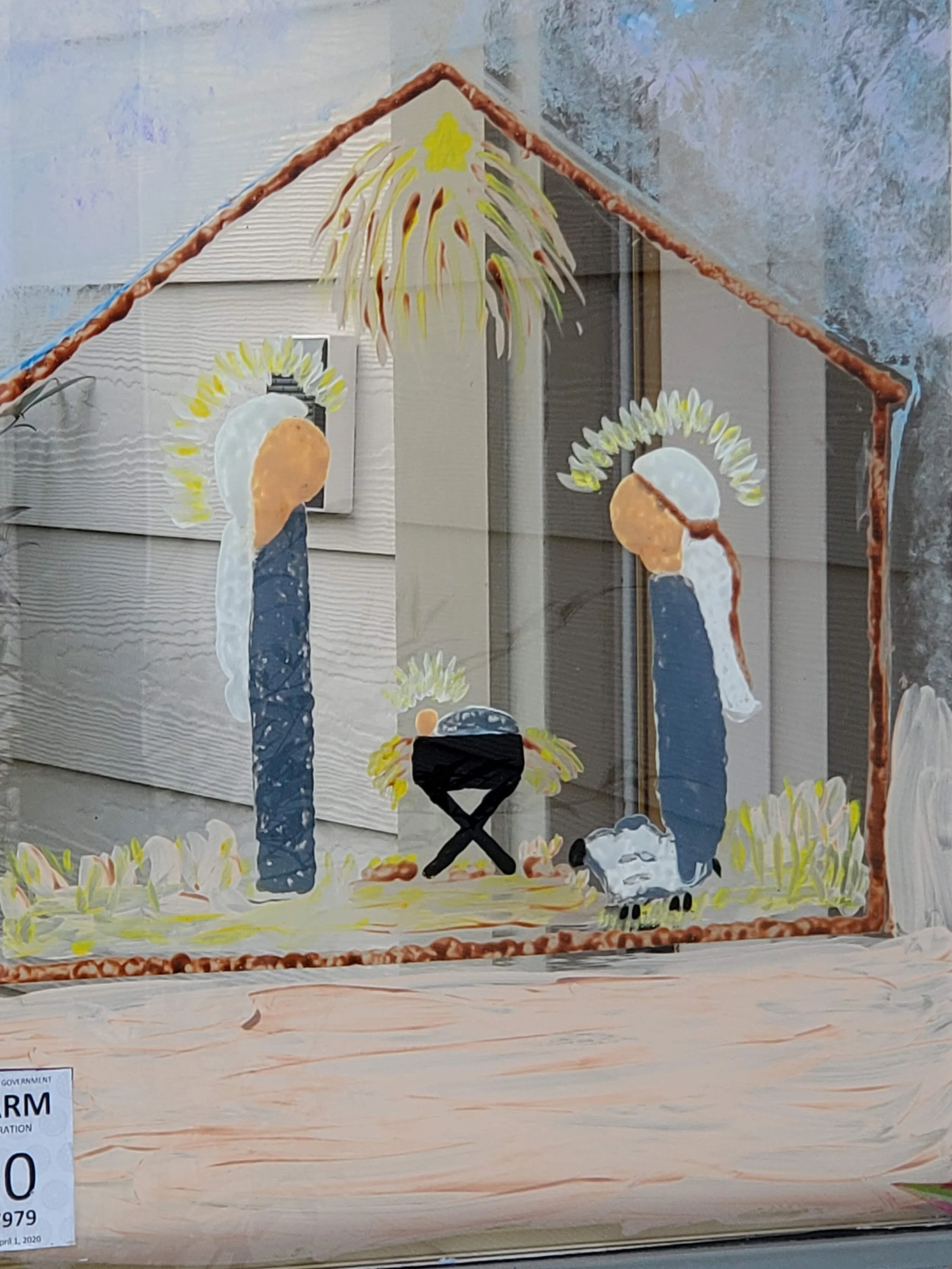 Painted window scene of a Nativity with Mary, Joseph, and baby Jesus in a manger. A sheep and star are also featured in the artwork.