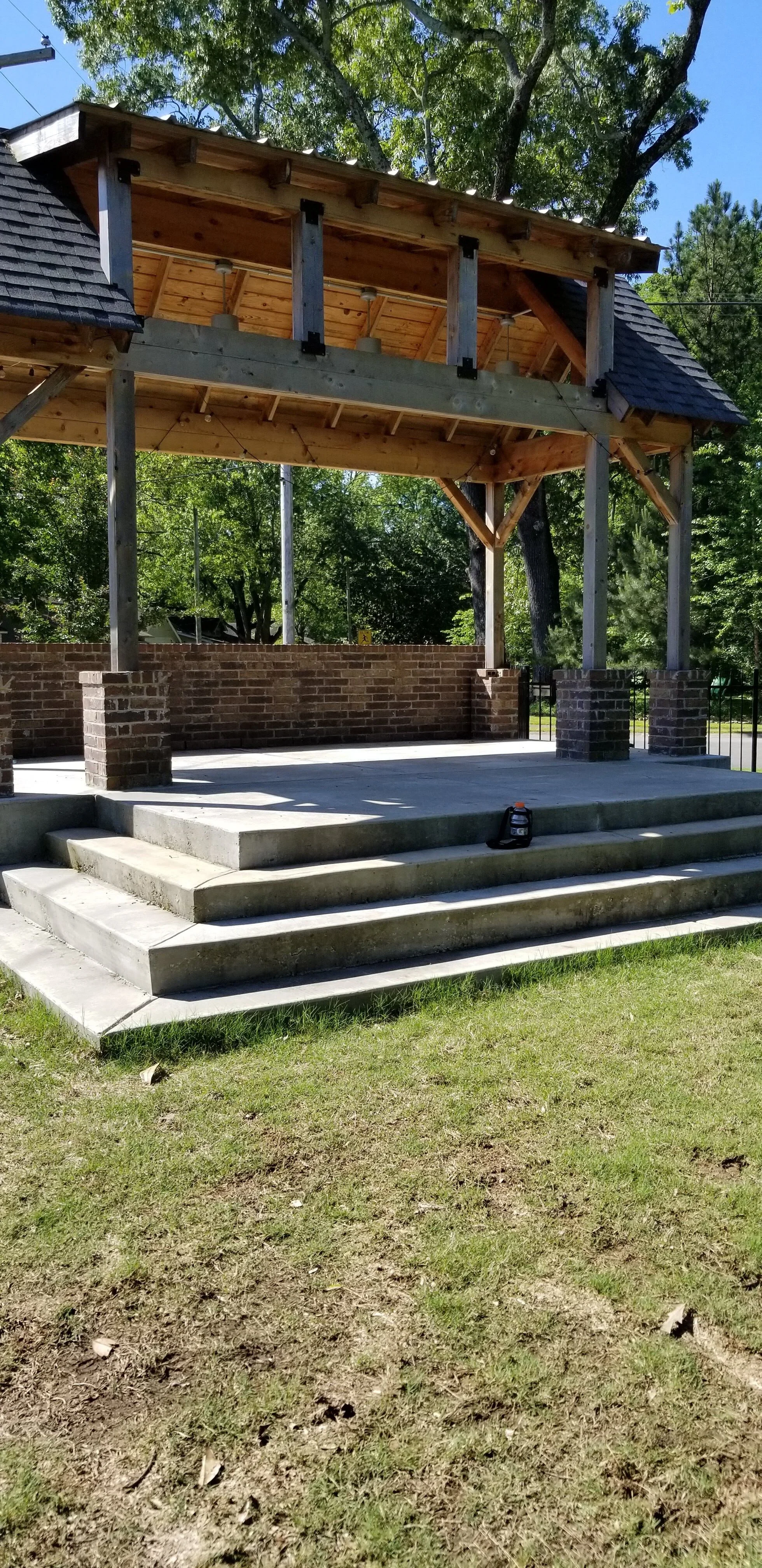 Outdoor wooden pavilion with brick and concrete steps, surrounded by trees.