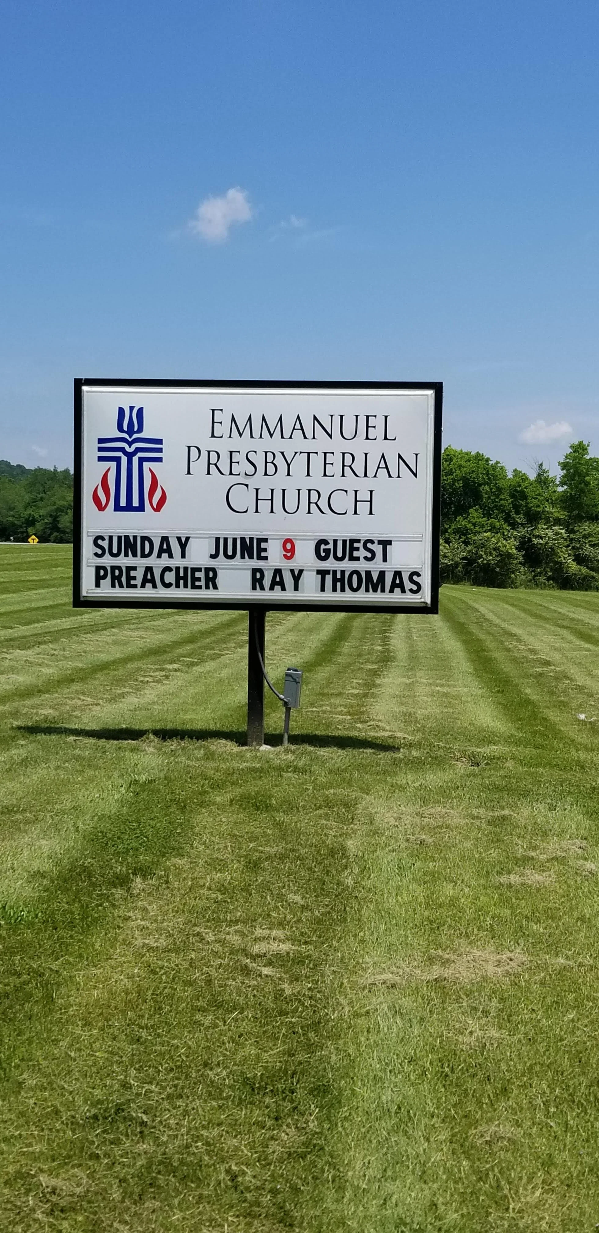 Sign outside Emmanuel Presbyterian Church, announcing guest preacher Ray Thomas for Sunday, June 9. The sign is on a grassy area with blue sky in the background.