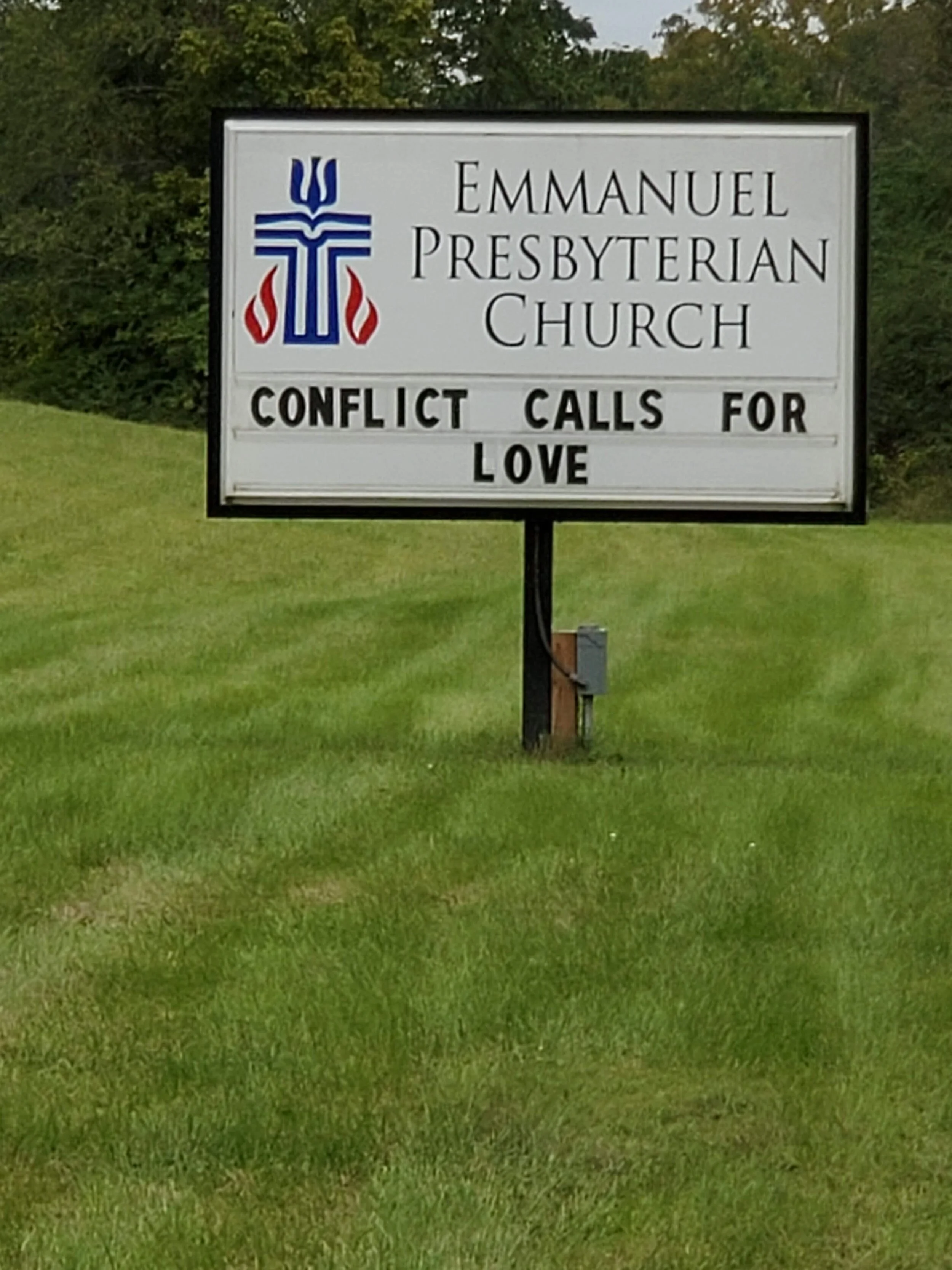 Church sign reading 'Emmanuel Presbyterian Church. Conflict calls for love' on grassy background.